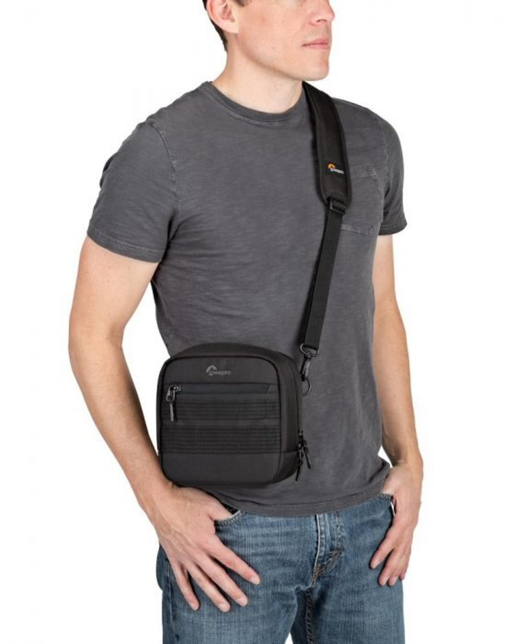 Ein Mann trägt eine schwarze Lowepro Kameratasche über dem Körper, Hände in den Taschen.