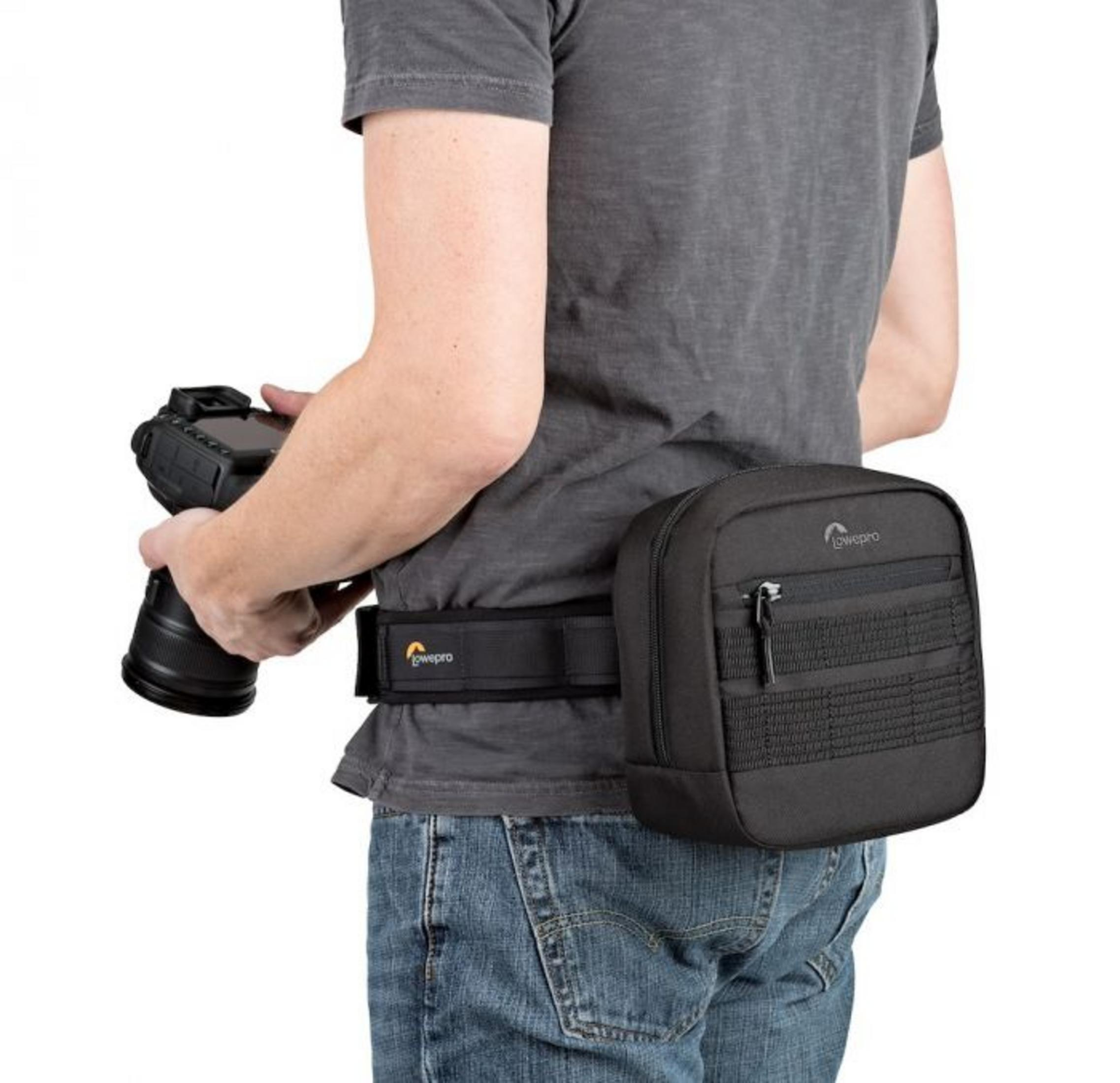 Person mit Hüfttasche und Kamera. Die Tasche ist schwarz, mit Markenlogo.