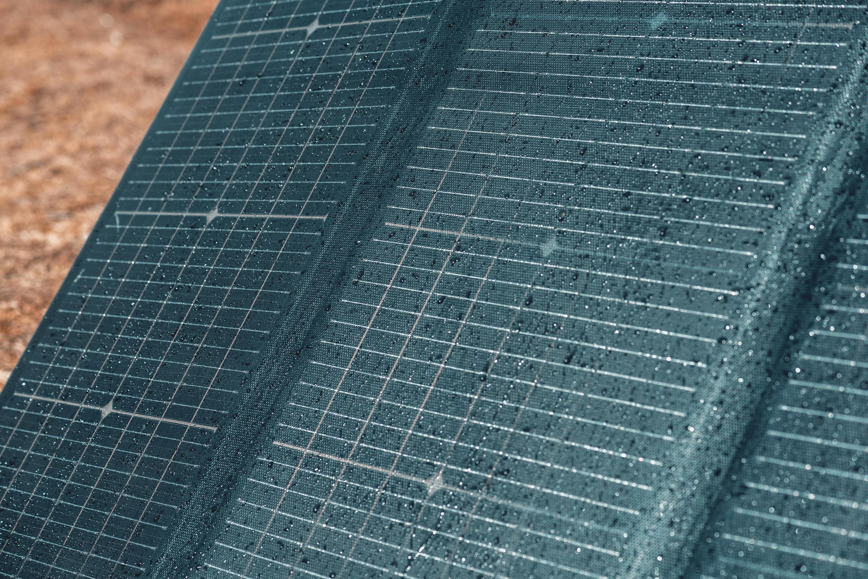 Zbliżenie na panel słoneczny z kroplami wody. Panel ma ciemne kwadraty.