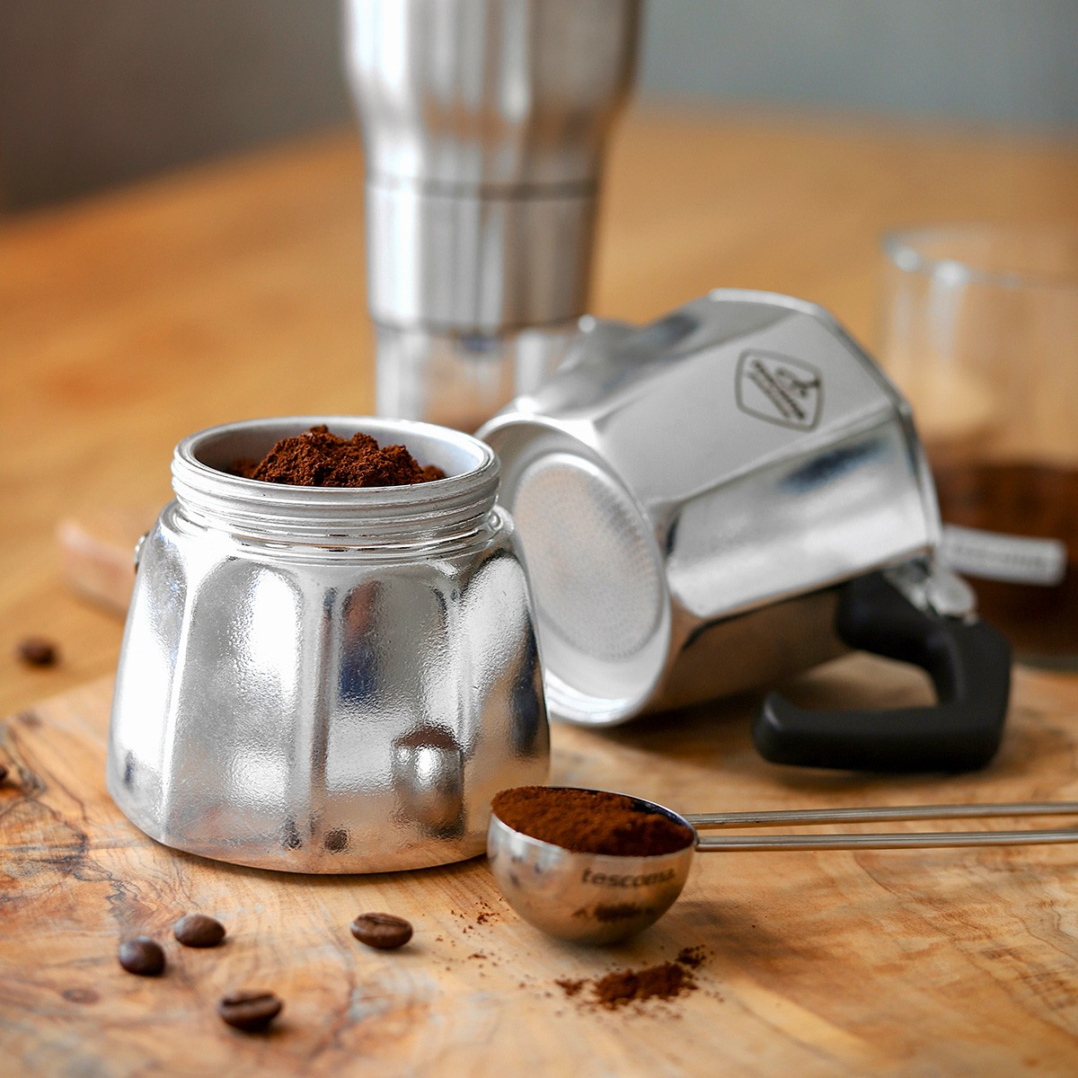 Metalowy ekspres do espresso z fusami kawy. Ziarna kawy i łyżka wypełniona kawą.