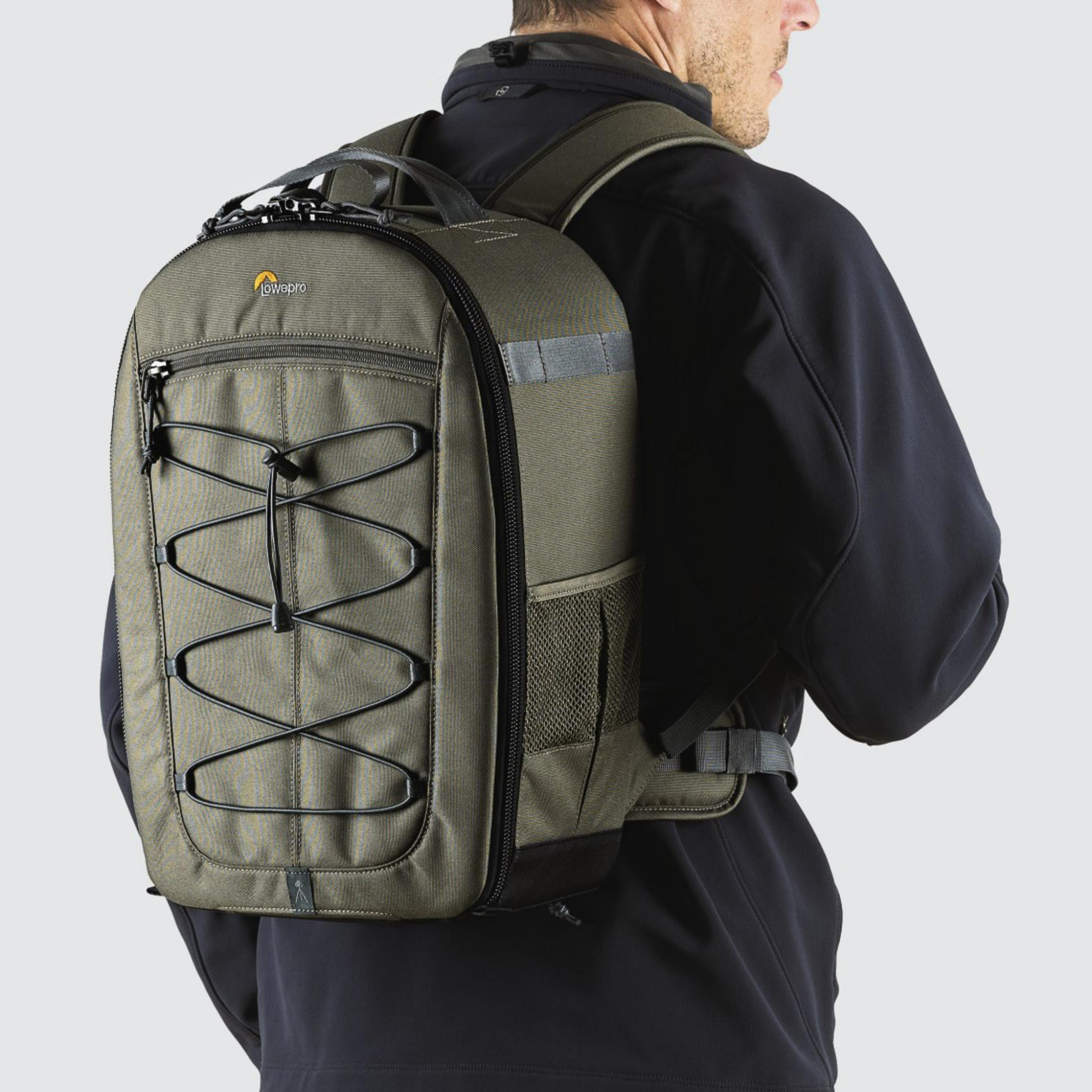 Ein Mann mit einem grünen Lowepro-Kamera-Rucksack. Er hat schwarze Bungee-Seile und einen Reißverschluss.