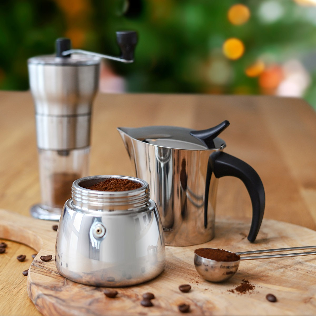 Kawiarka, młynek i łyżka ze stali nierdzewnej na drewnianej desce z ziarnami kawy.