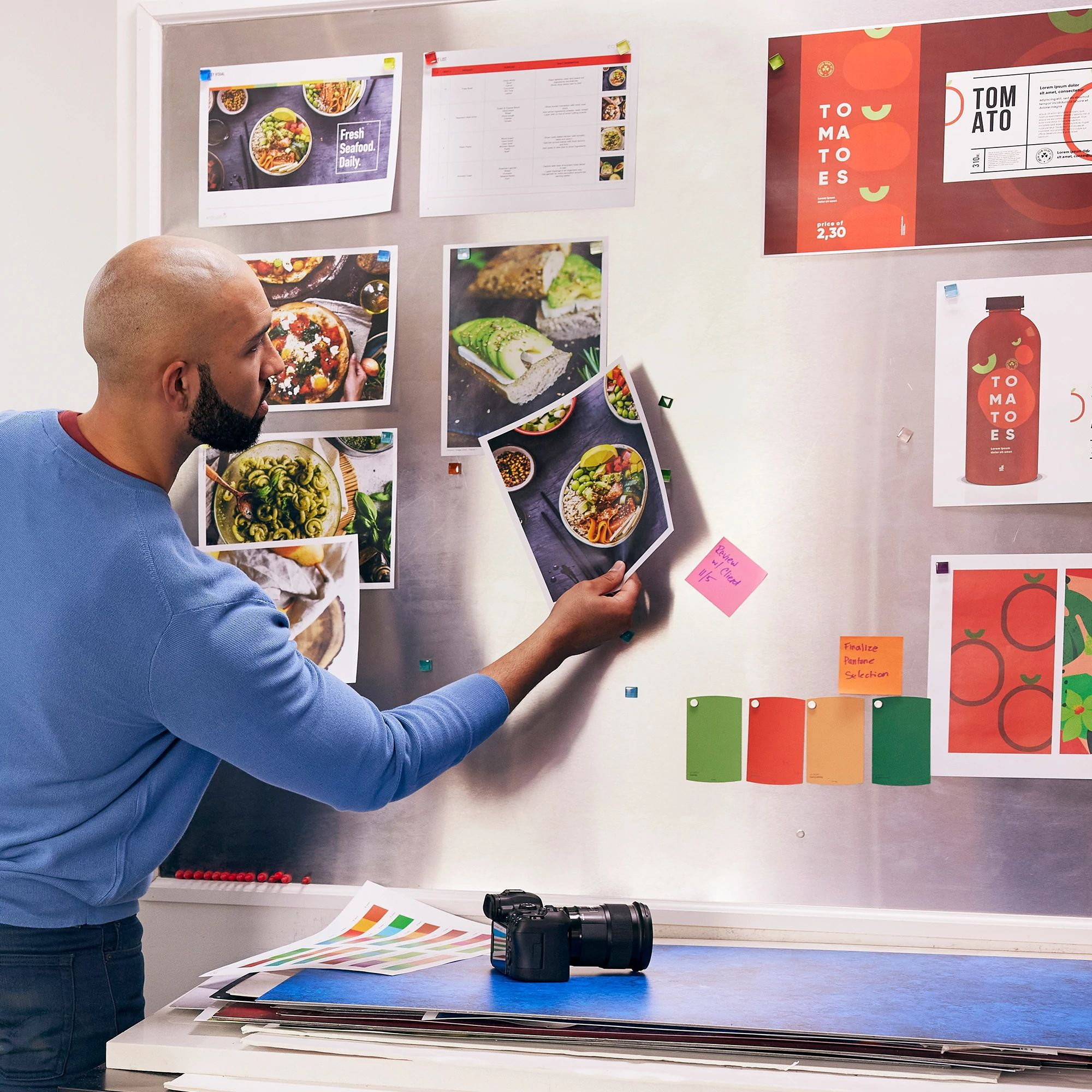 Ein Mann betrachtet Fotos auf einer Metalltafel. Fotos zeigen Essen und Designelemente.
