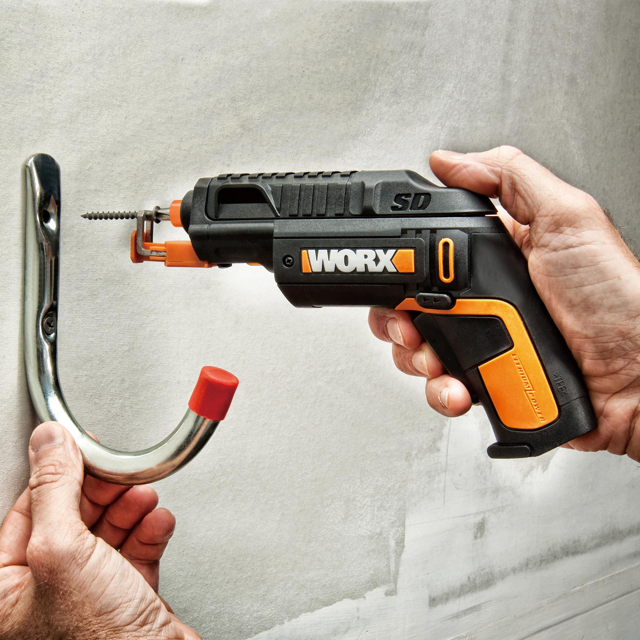 Osoba używająca czarno-pomarańczowej wiertarki akumulatorowej do przymocowania haka do jasnoszarej ściany.