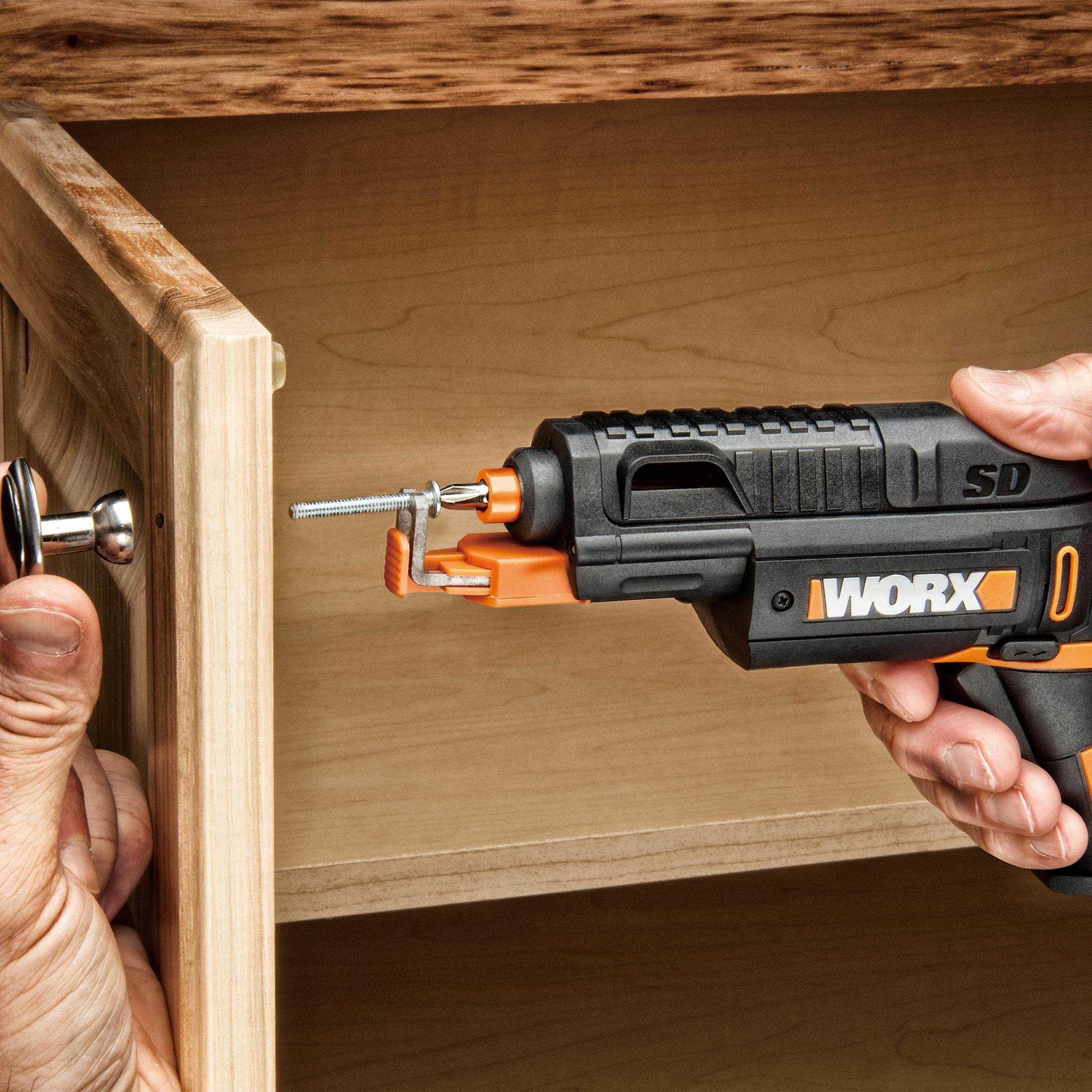 Osoba używająca czarno-pomarańczowej wiertarki do drewna, celująca w szafkę.