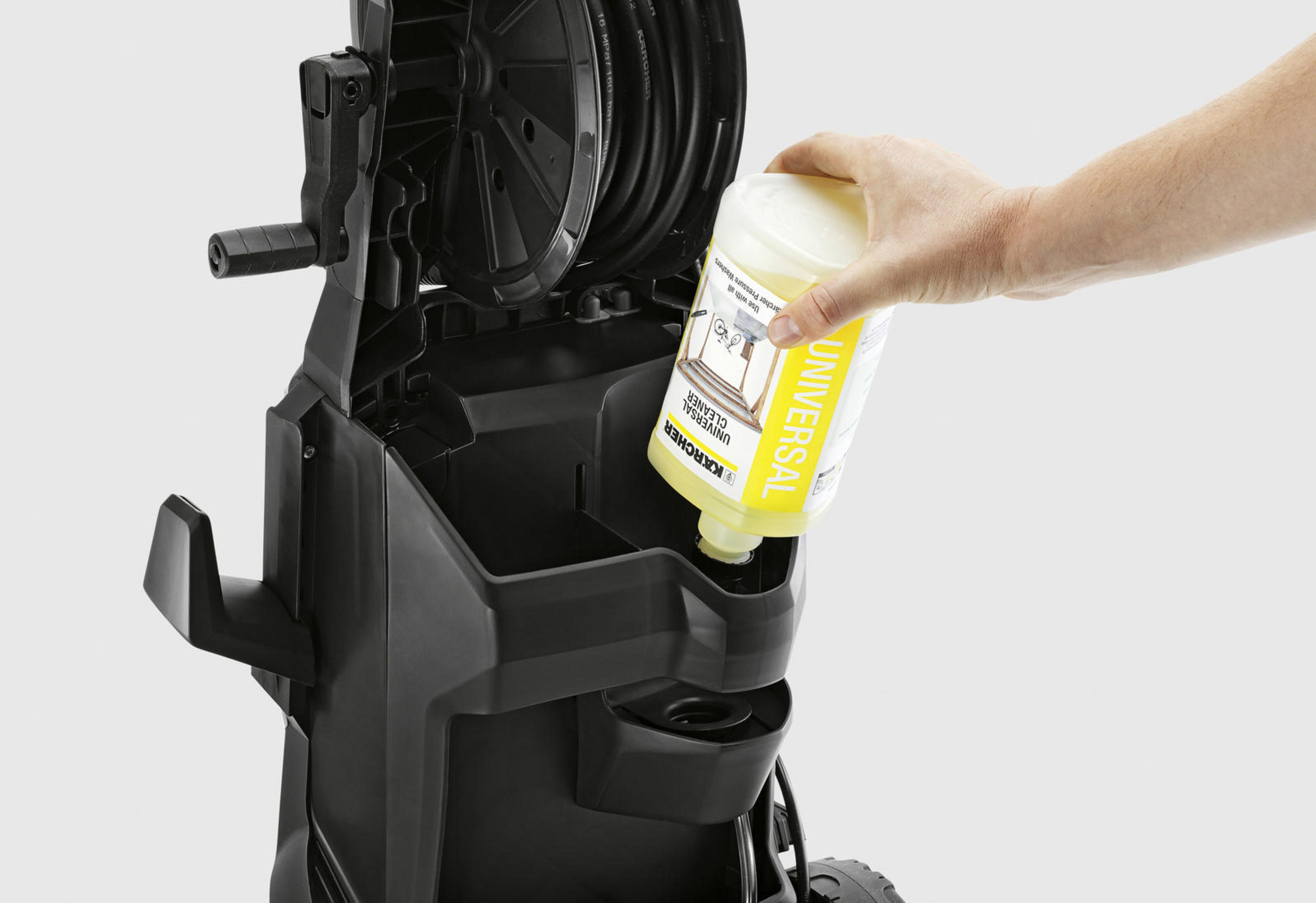 Person pouring yellow cleaner into a pressure washer. The washer is black. White background.