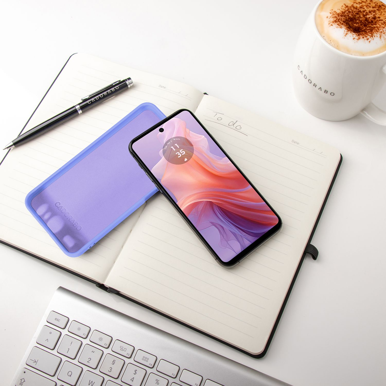 Telefon und Hülle auf einem Notizbuch mit Stift und Kaffee. Tastatur im Vordergrund. Weißer Hintergrund.