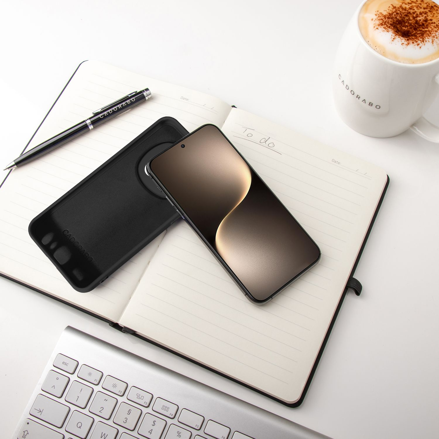 Eine Handyhülle und ein Telefon liegen auf einem Notizbuch, mit Stift und Kaffeetasse.