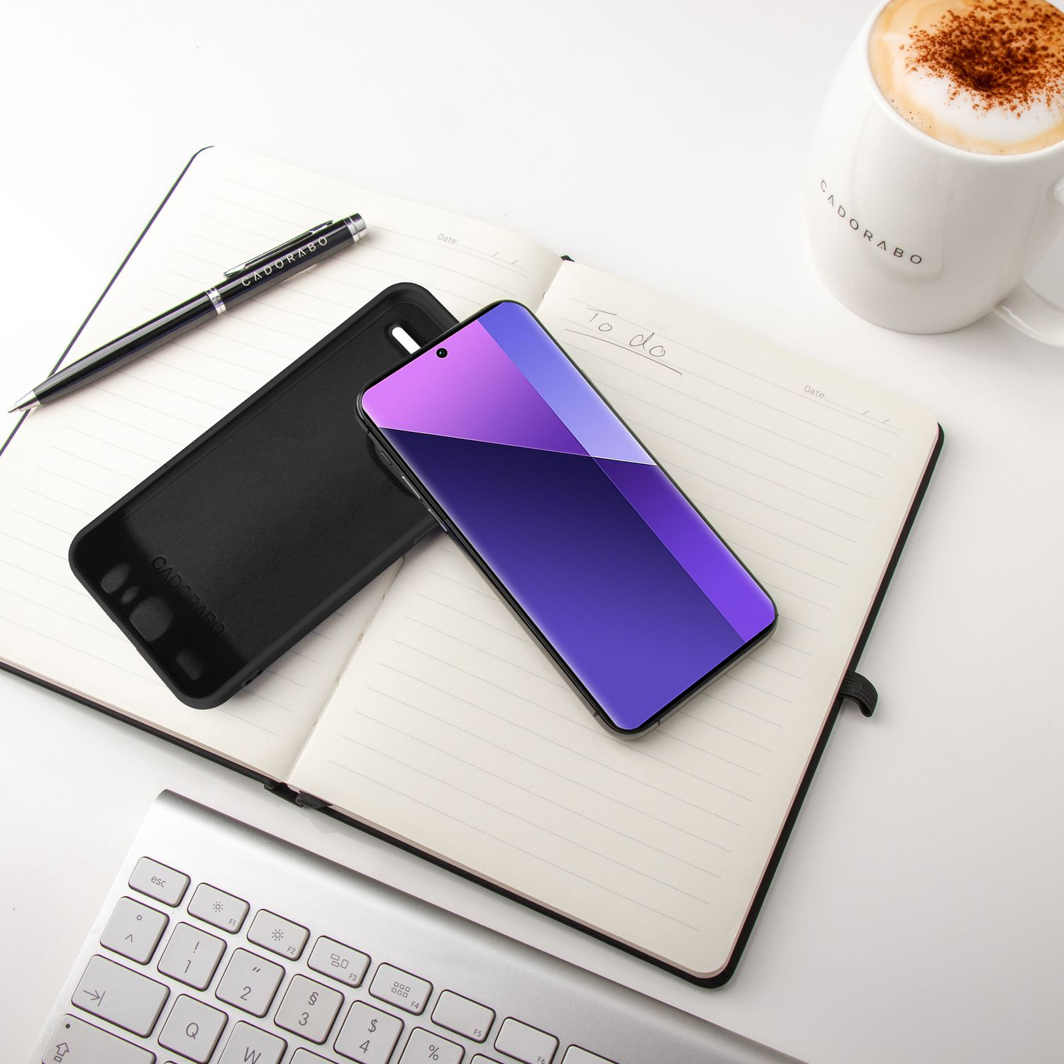 Schwarze Handyhülle und Telefon liegen auf einem Notizbuch. Ein Stift und eine Kaffeetasse liegen ebenfalls auf dem Schreibtisch.