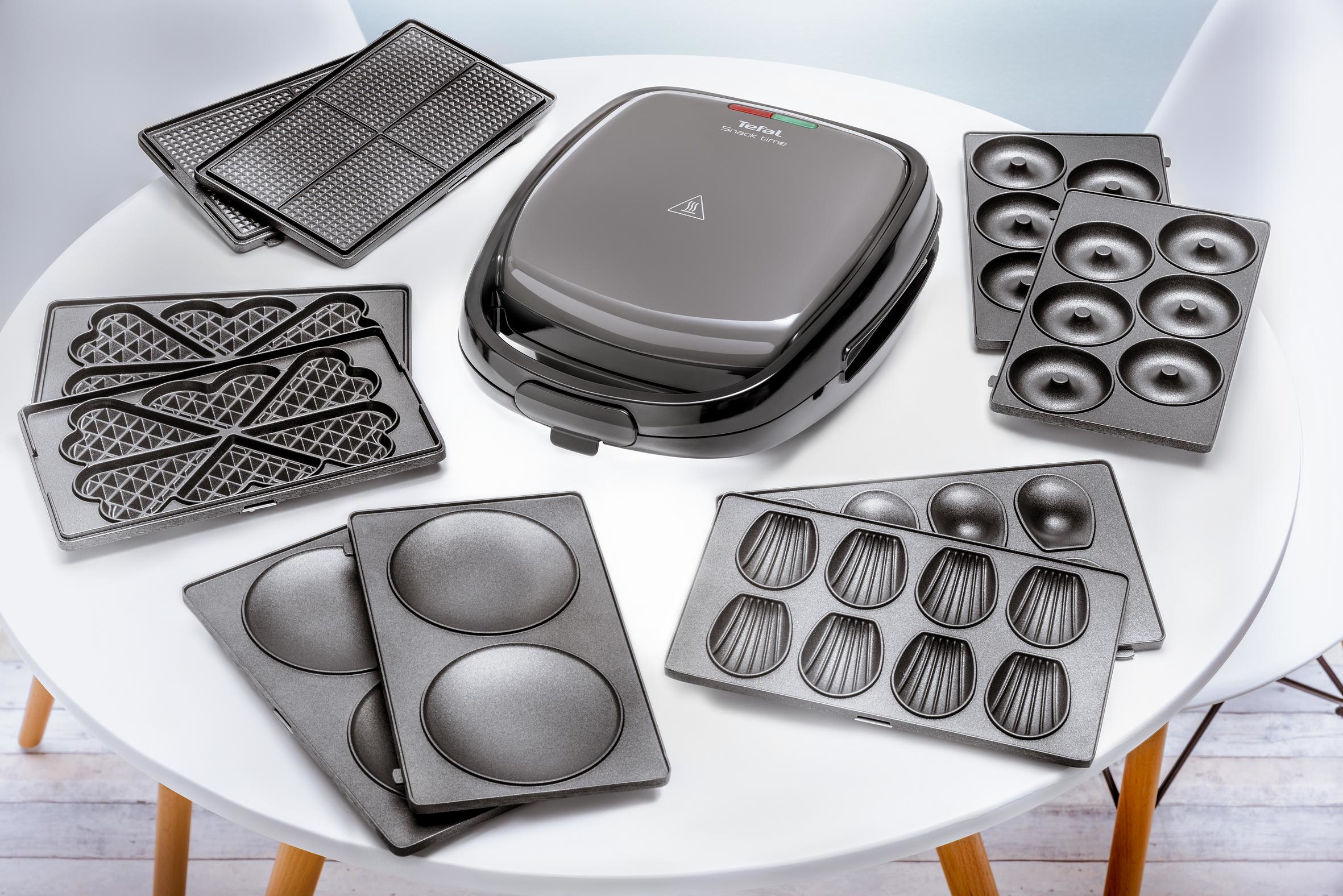 Various baking plates on a white table, with a closed black appliance in the center.
