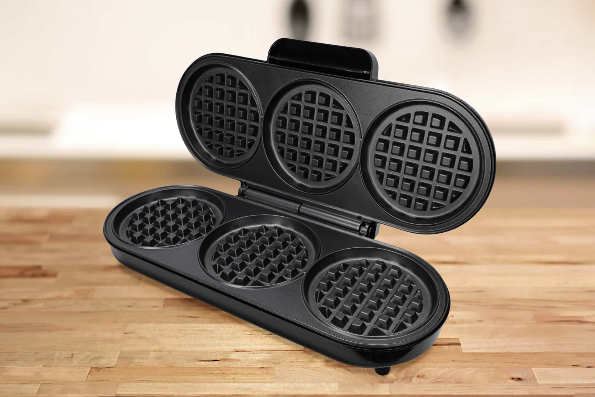 Czarny gofrownica otwarty, pokazujący trzy formy do gofrów. Jest na drewnianym stole.