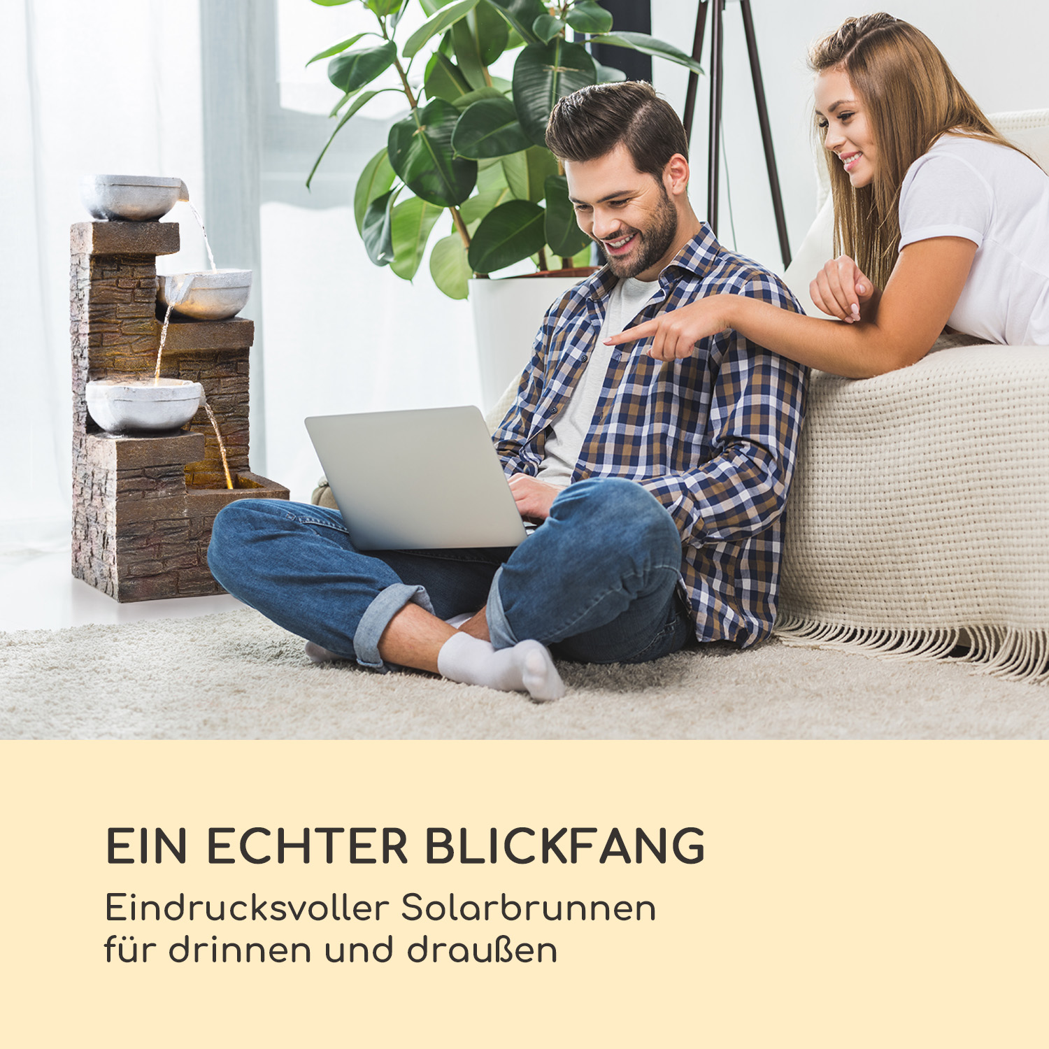 Ein Paar betrachtet Laptop, vor einem Springbrunnen sitzend.