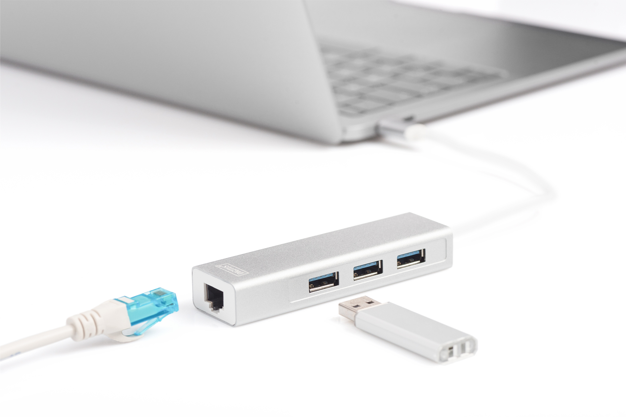 Silberner USB-Hub, verbunden mit einem Laptop und einem USB-Laufwerk auf weißer Oberfläche.