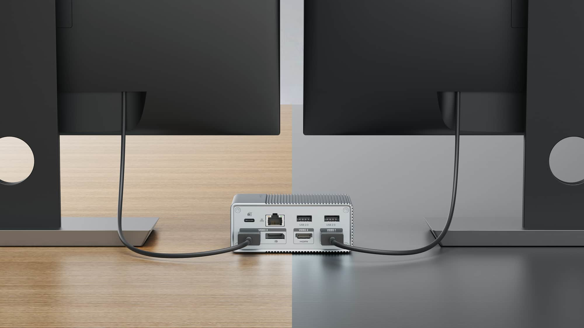 Un piccolo dispositivo argentato con molte porte di ingresso collegato a due monitor.