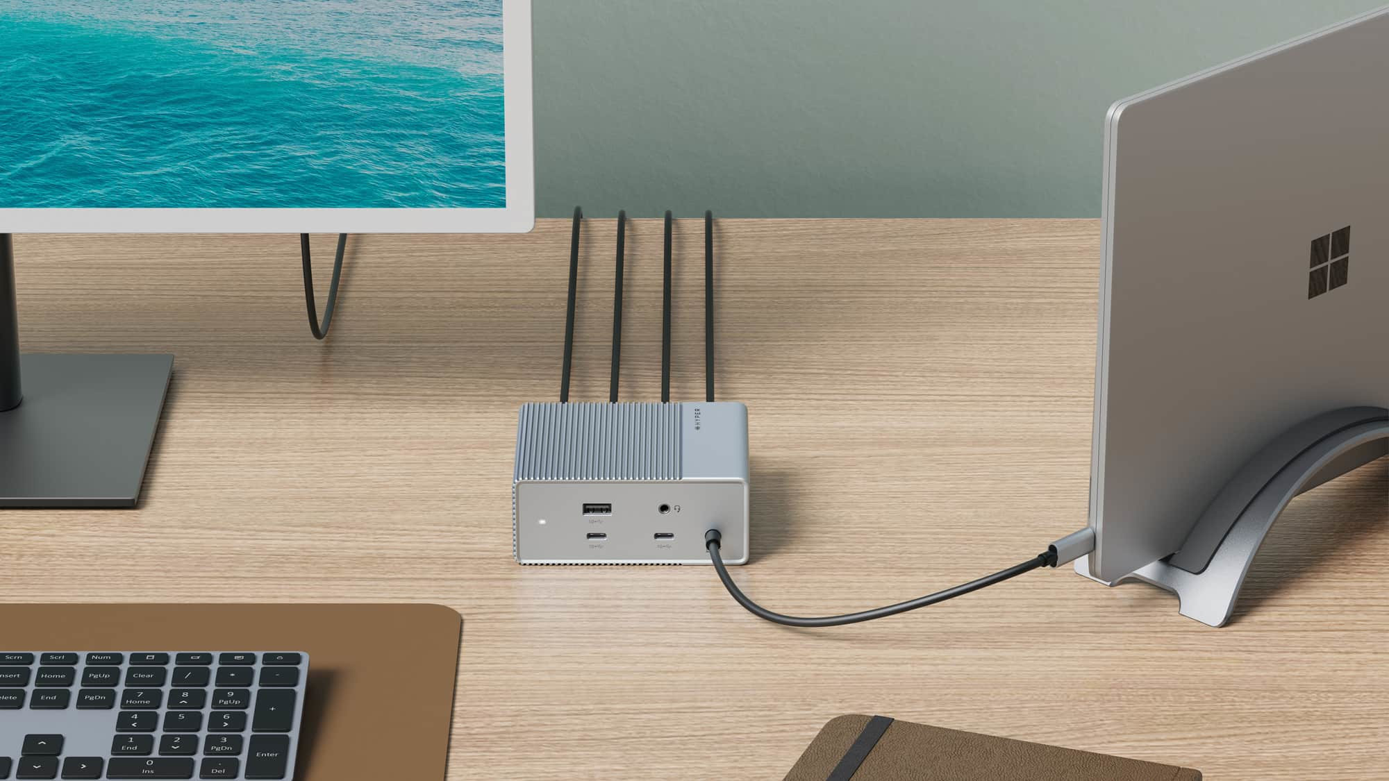 Configurazione scrivania con monitor, laptop e docking station con cavi, su superficie di legno.