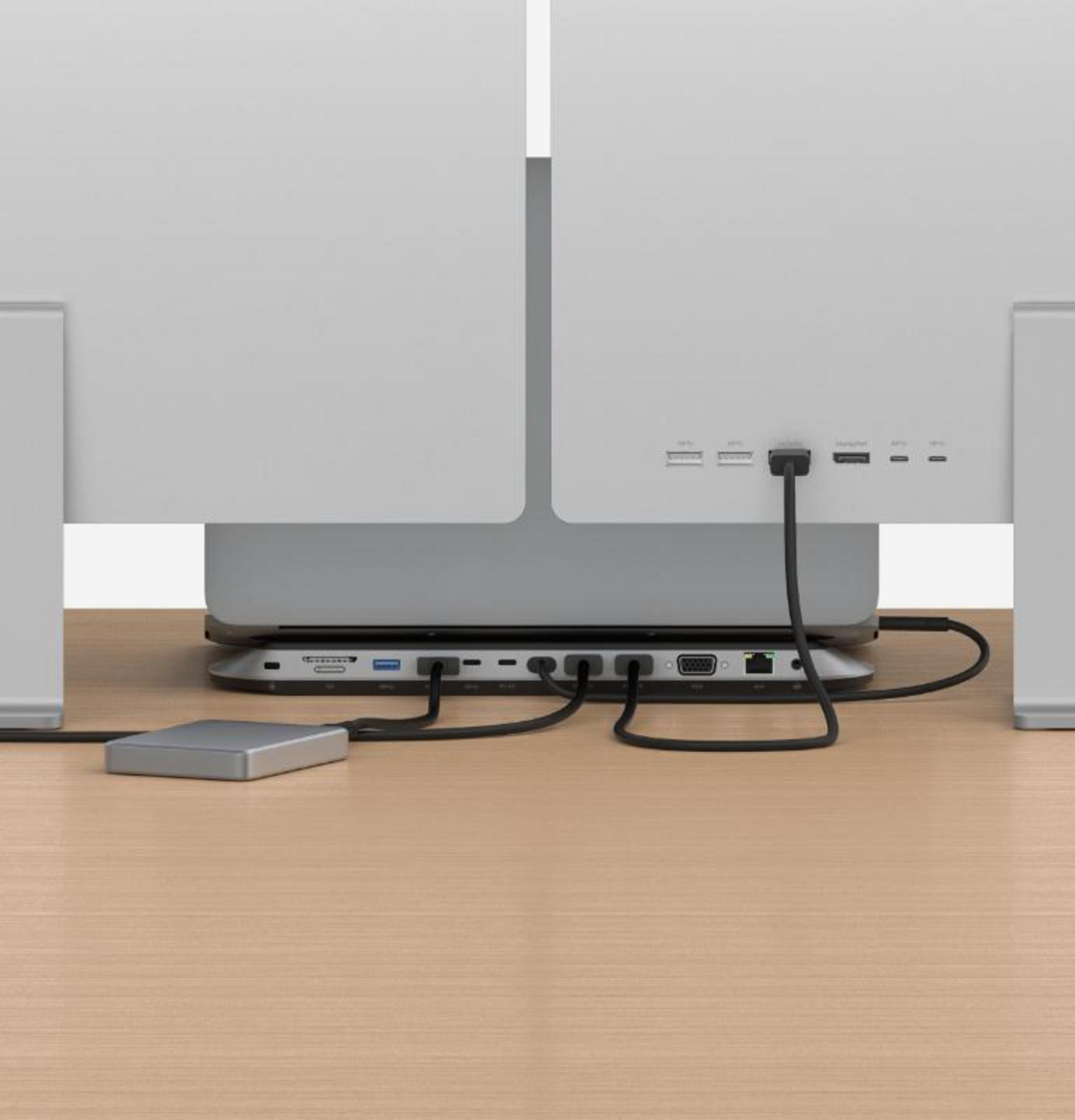 Ein Schreibtisch-Setup mit zwei Monitoren. Kabel sind mit einem Hub verbunden, der sich auf dem Schreibtisch befindet.