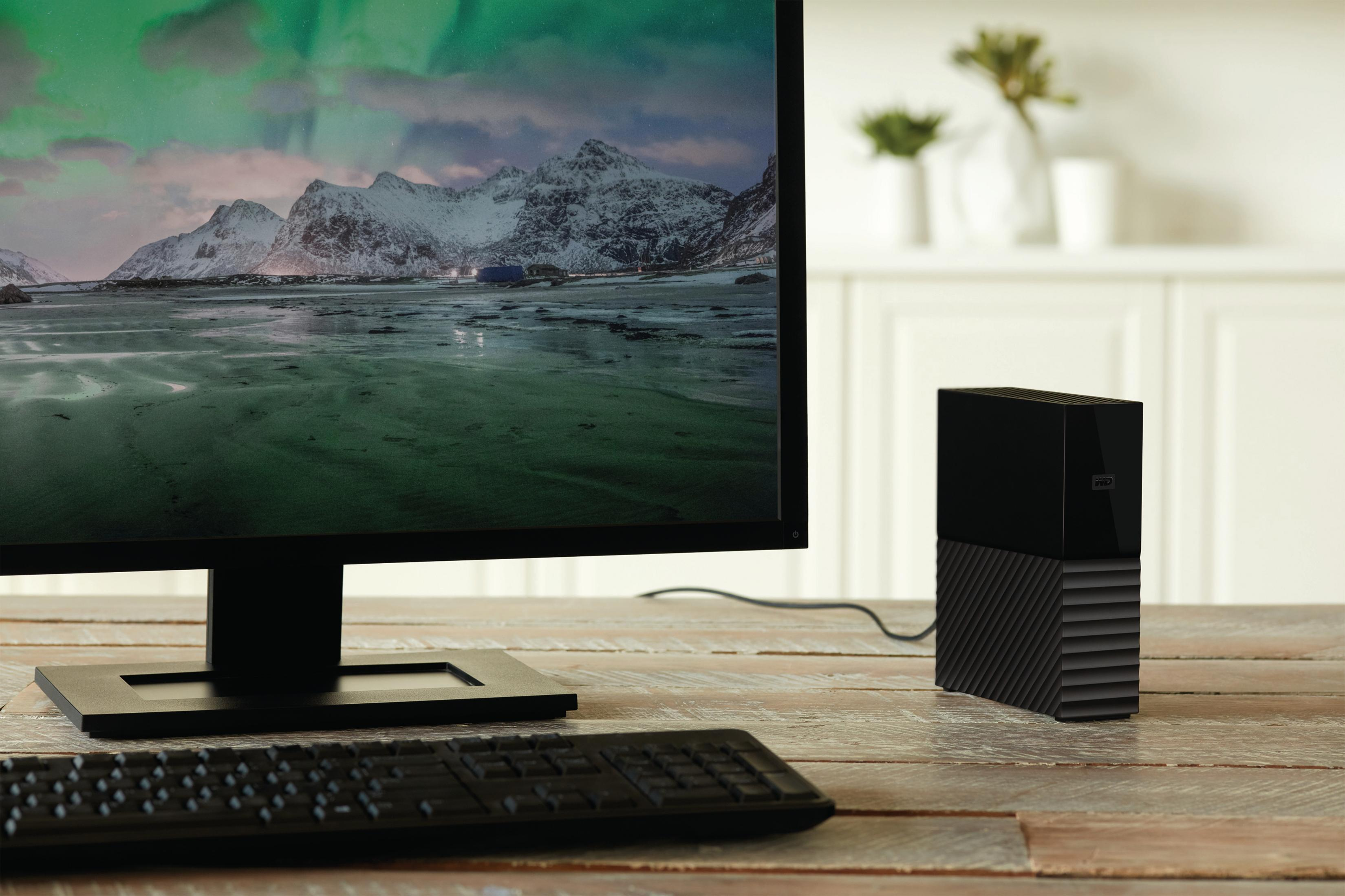 Monitor, komputer i klawiatura na drewnianym biurku. Monitor wyświetla krajobraz.