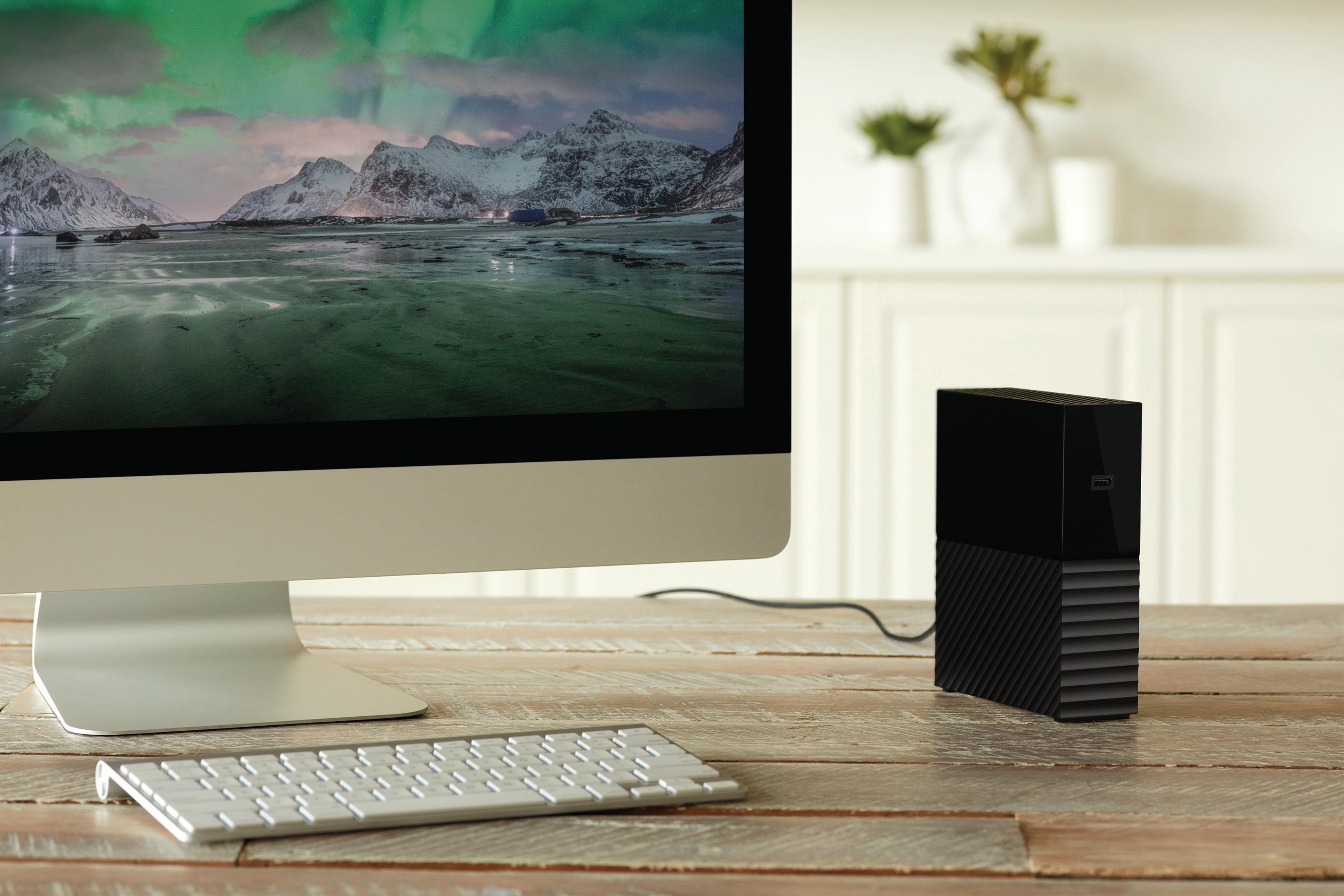 Monitor komputera wyświetlający krajobraz. Czarny zewnętrzny dysk twardy obok na drewnianym biurku.