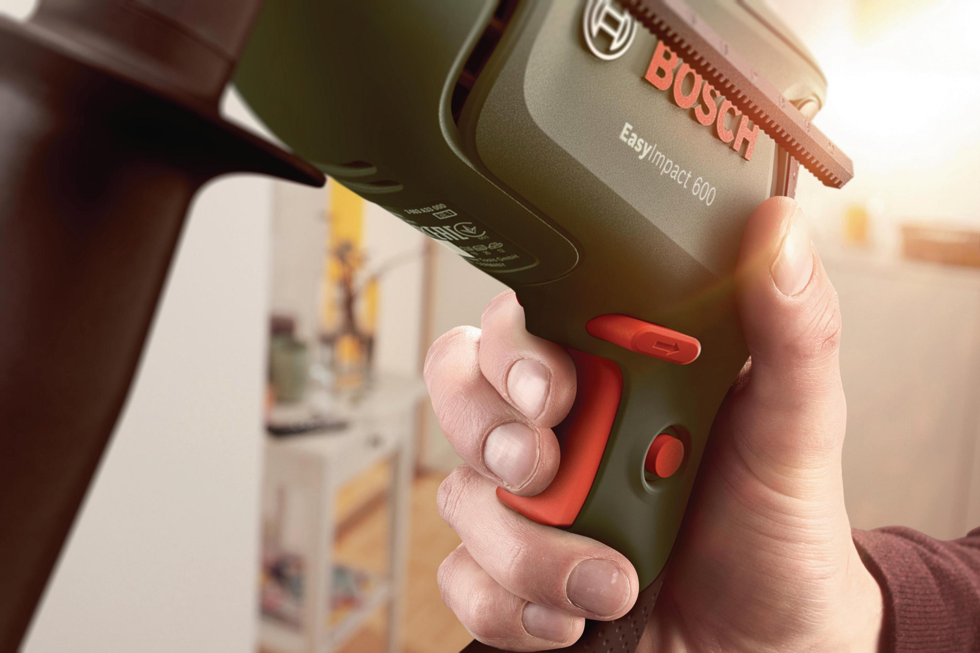 Una mano sostiene un taladro verde Bosch EasyImpact 600, mostrando sus botones naranjas y etiqueta roja.