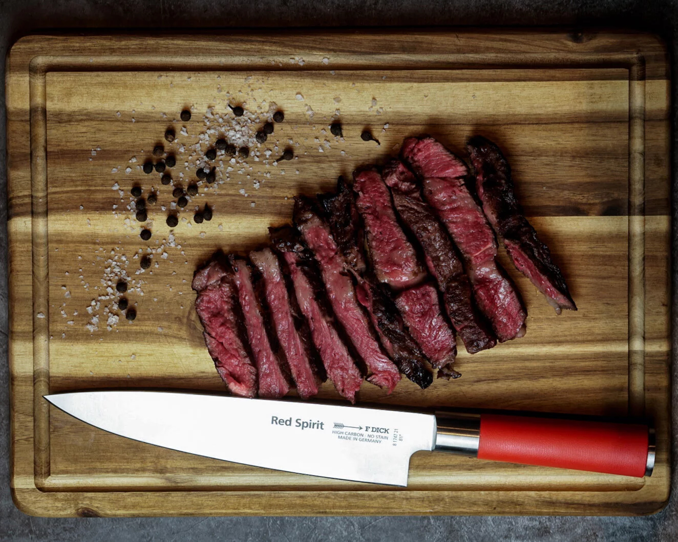 Geschnittenes Steak auf einem Holzbrett. Messer und Pfeffer daneben. Red Spirit Messer.