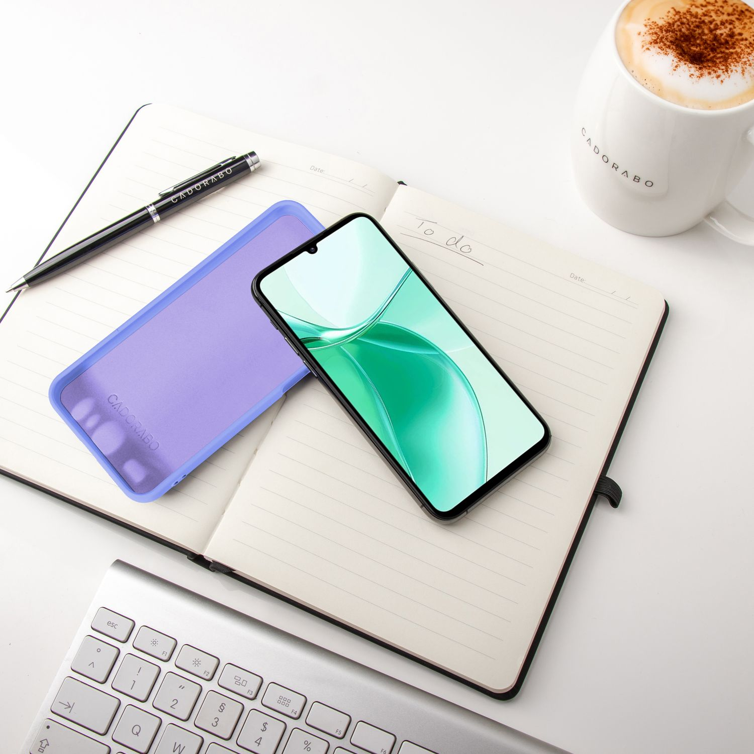 Notizbuch, Stift, Telefon und Hülle auf weißer Oberfläche. Latte-Tasse und Tastatur vorhanden.