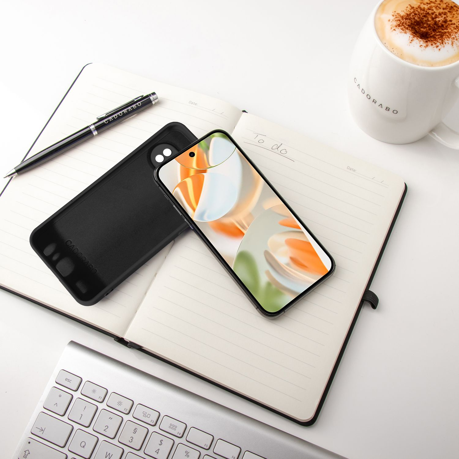 Schwarzes Telefon mit Hülle auf einem Notizbuch. Stift, Kaffee und Tastatur. Weißer Hintergrund.