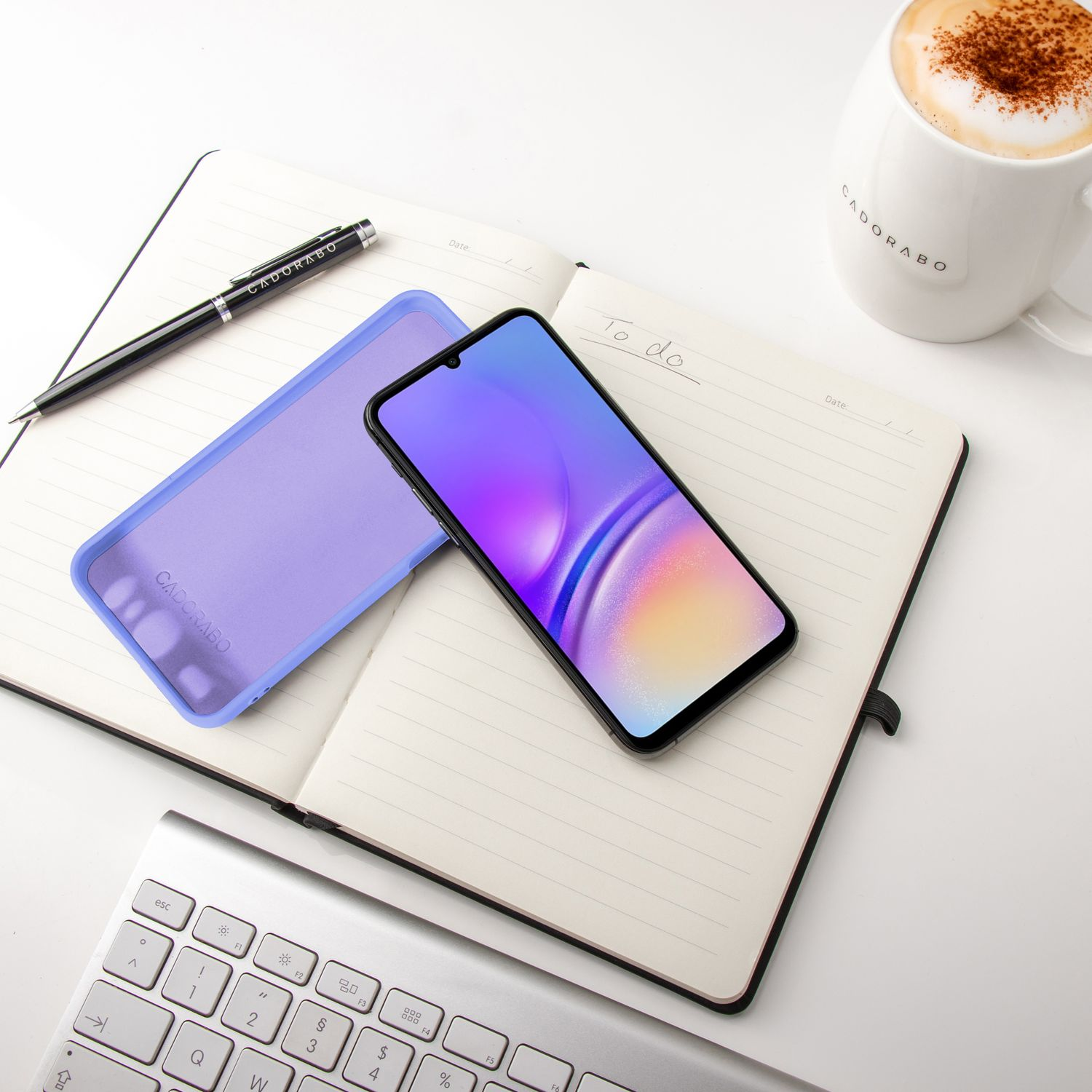 Notizbuch mit Telefon, Hülle, Stift und Kaffeetasse auf weißer Oberfläche.