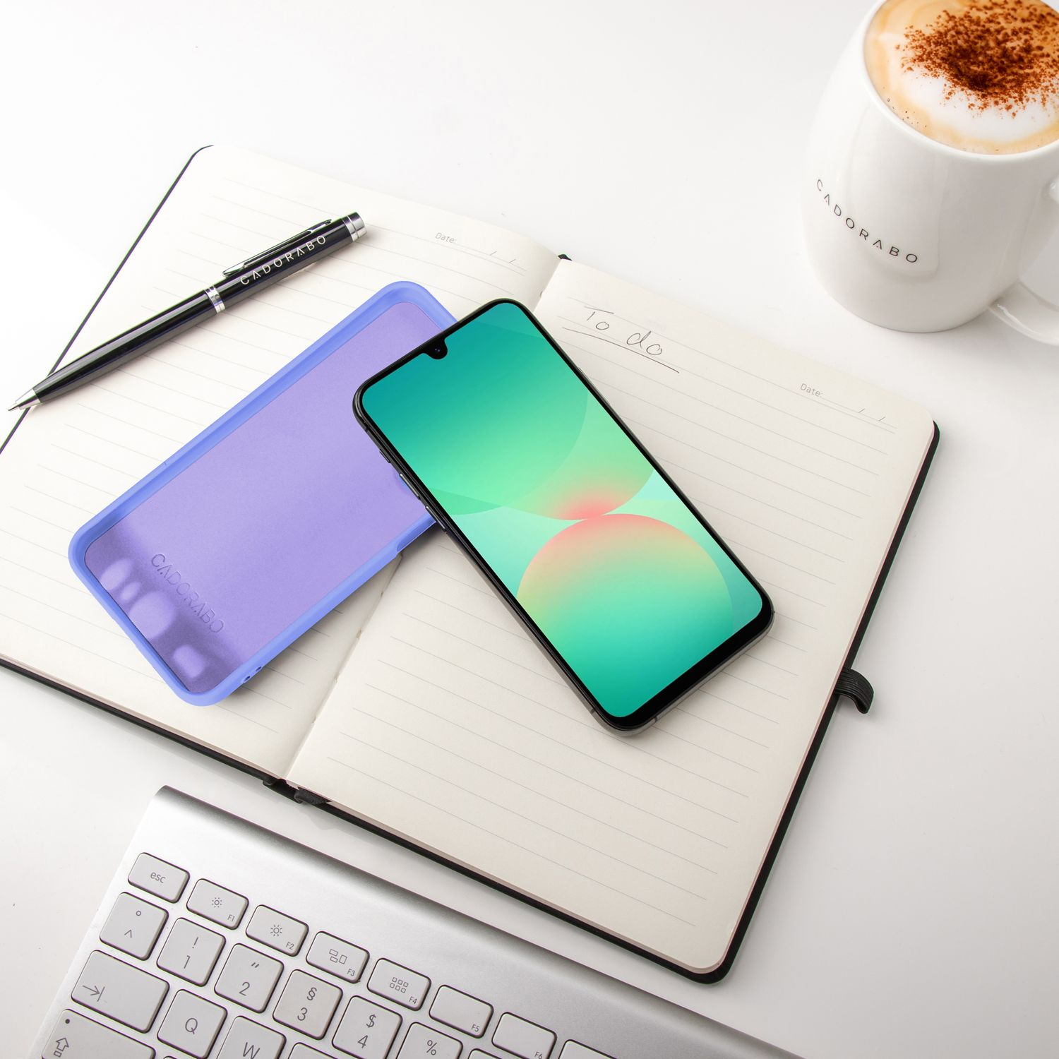 Notizbuch geöffnet mit Telefon und Hülle, Stift und Kaffee.