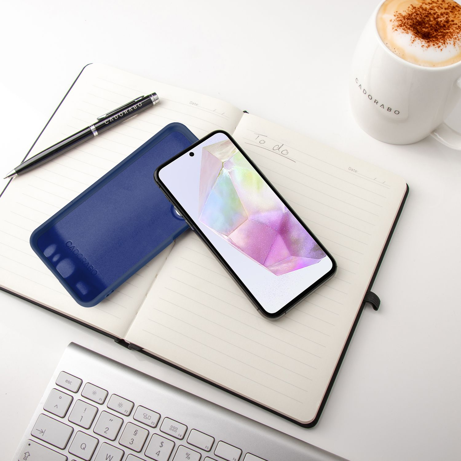 Notizbuch geöffnet mit Telefon und blauer Hülle, Stift und Kaffee.