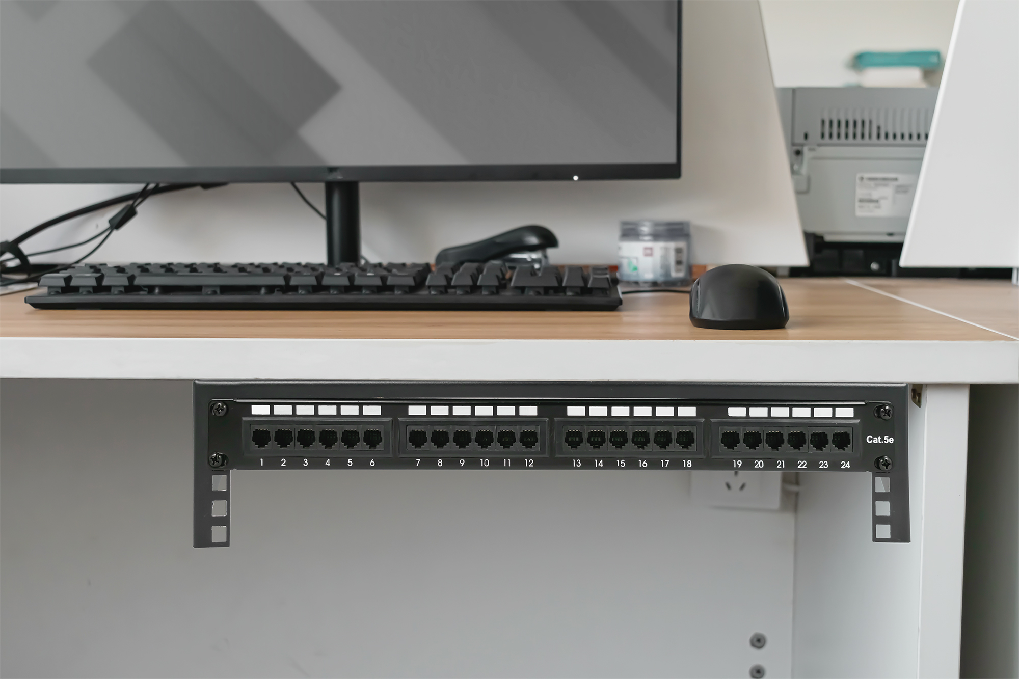 Czarny panel krosowy sieci zainstalowany pod biurkiem, z ponumerowanymi portami.