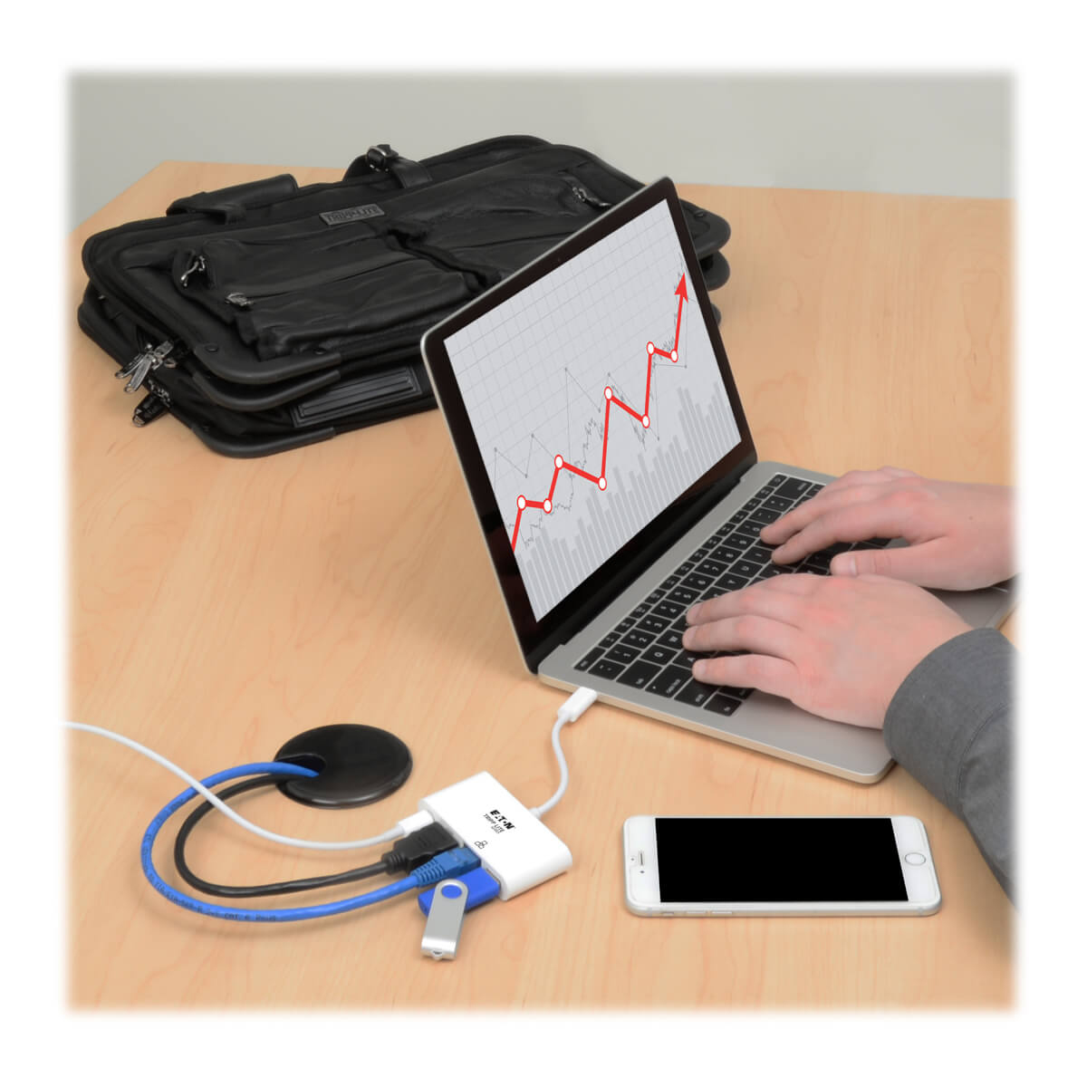 Laptop podłączony do białej przejściówki z portami USB, HDMI i USB-C. Obok leży telefon.