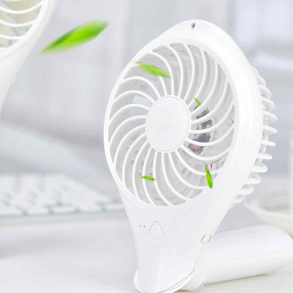 Weißer Handventilator mit Windblättern, mit grünen Blättern, die in der Luft schweben.