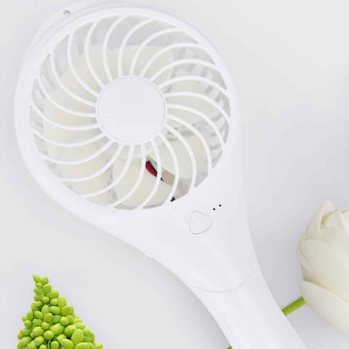 Weißer Handventilator mit Griff und Blume. Der Ventilator hat einen Knopf und einen runden Kopf.
