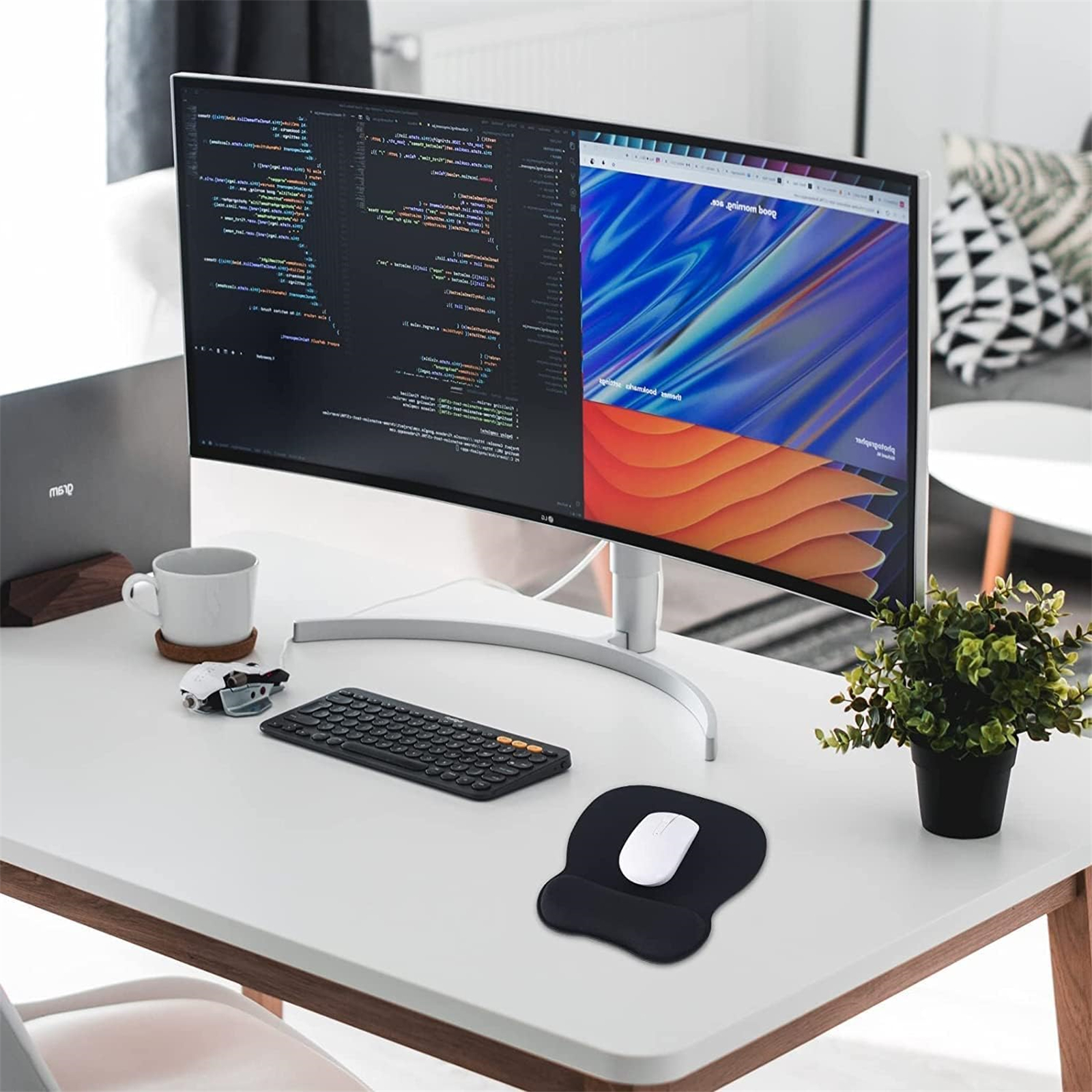 Ein Schreibtisch mit Monitor, Tastatur, Maus und Pflanze. Ein Laptop und eine Tasse sind ebenfalls vorhanden.