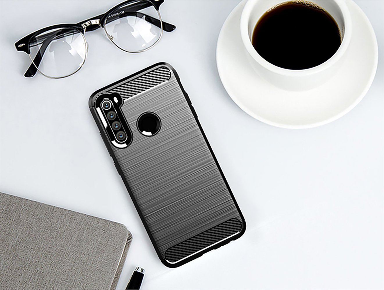 Teléfono negro sobre una superficie blanca con gafas, un bloc de notas y una taza de café.
