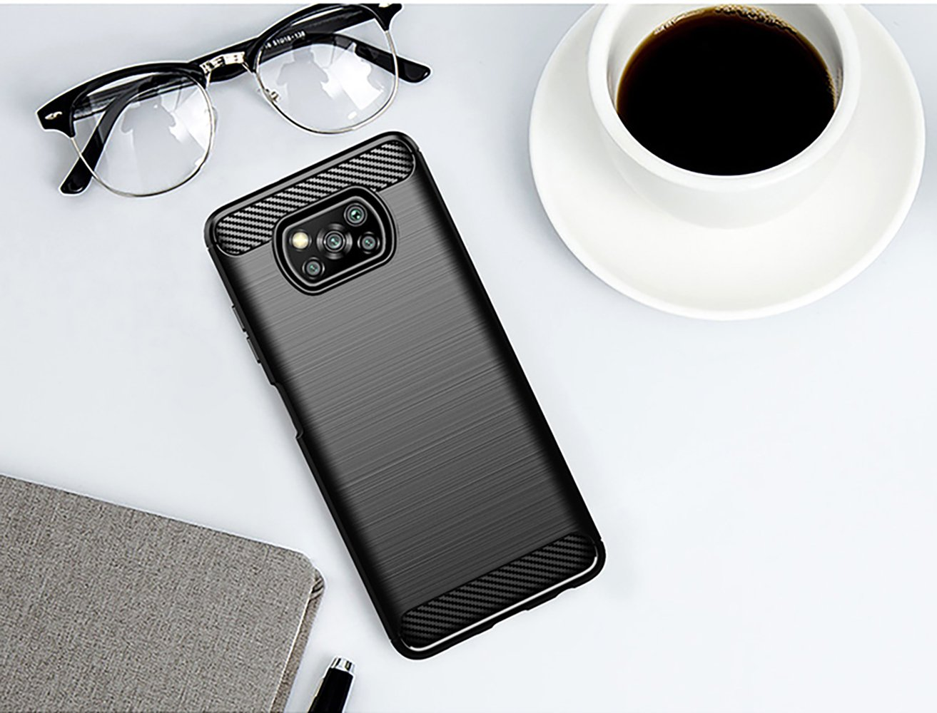 Funda negra con textura, gafas, taza de café y cuaderno sobre superficie blanca.
