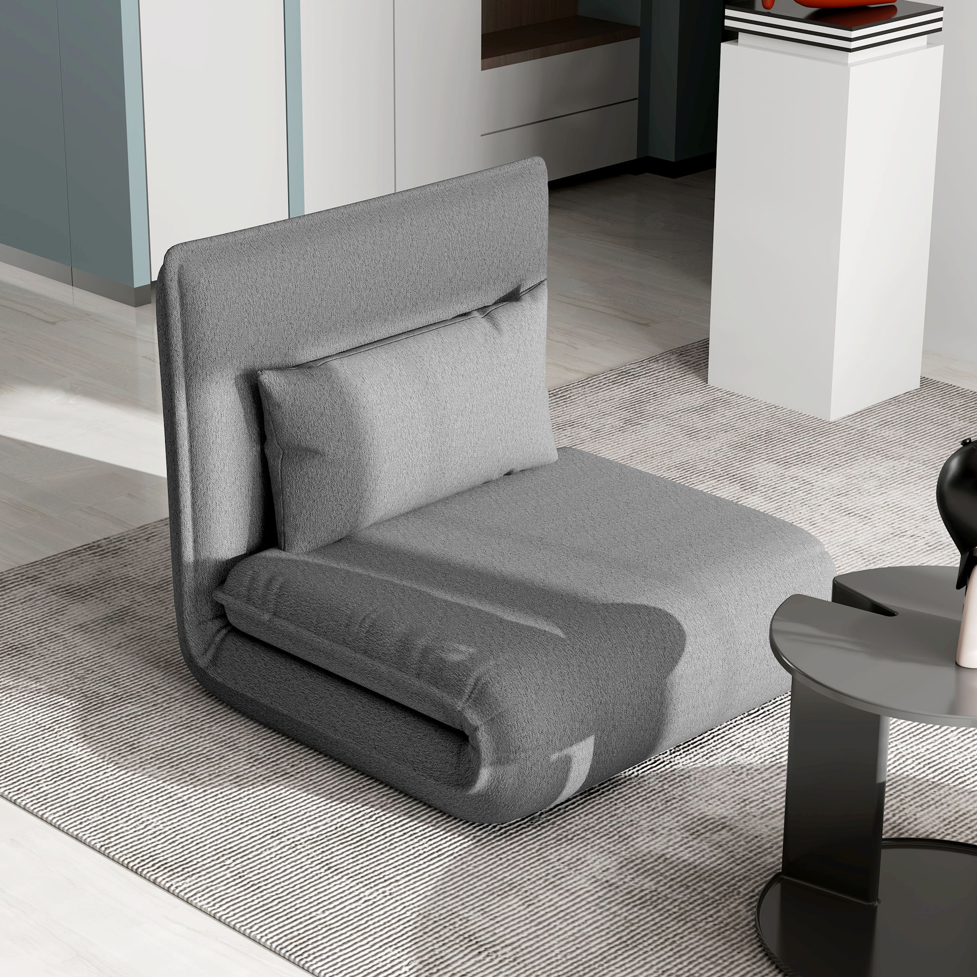 Ein graues Stuhl-Bett in einem Raum mit Teppich und kleinem Tisch.