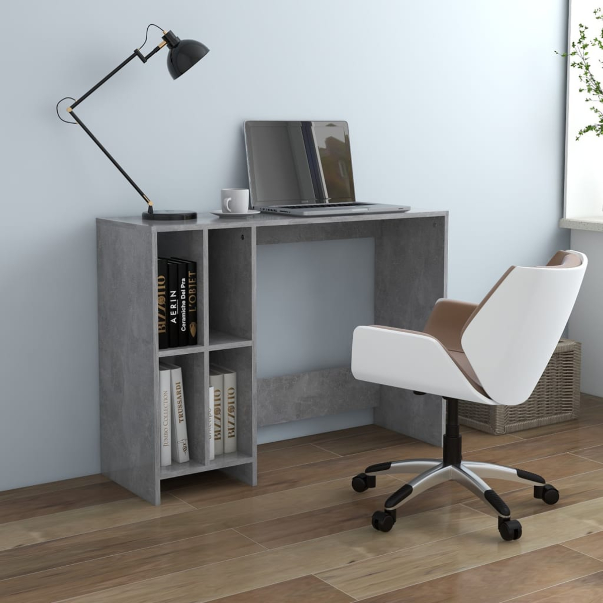 Ein grauer Schreibtisch mit Laptop, Lampe und Stuhl. Bücher liegen auf der Seite des Schreibtischs.