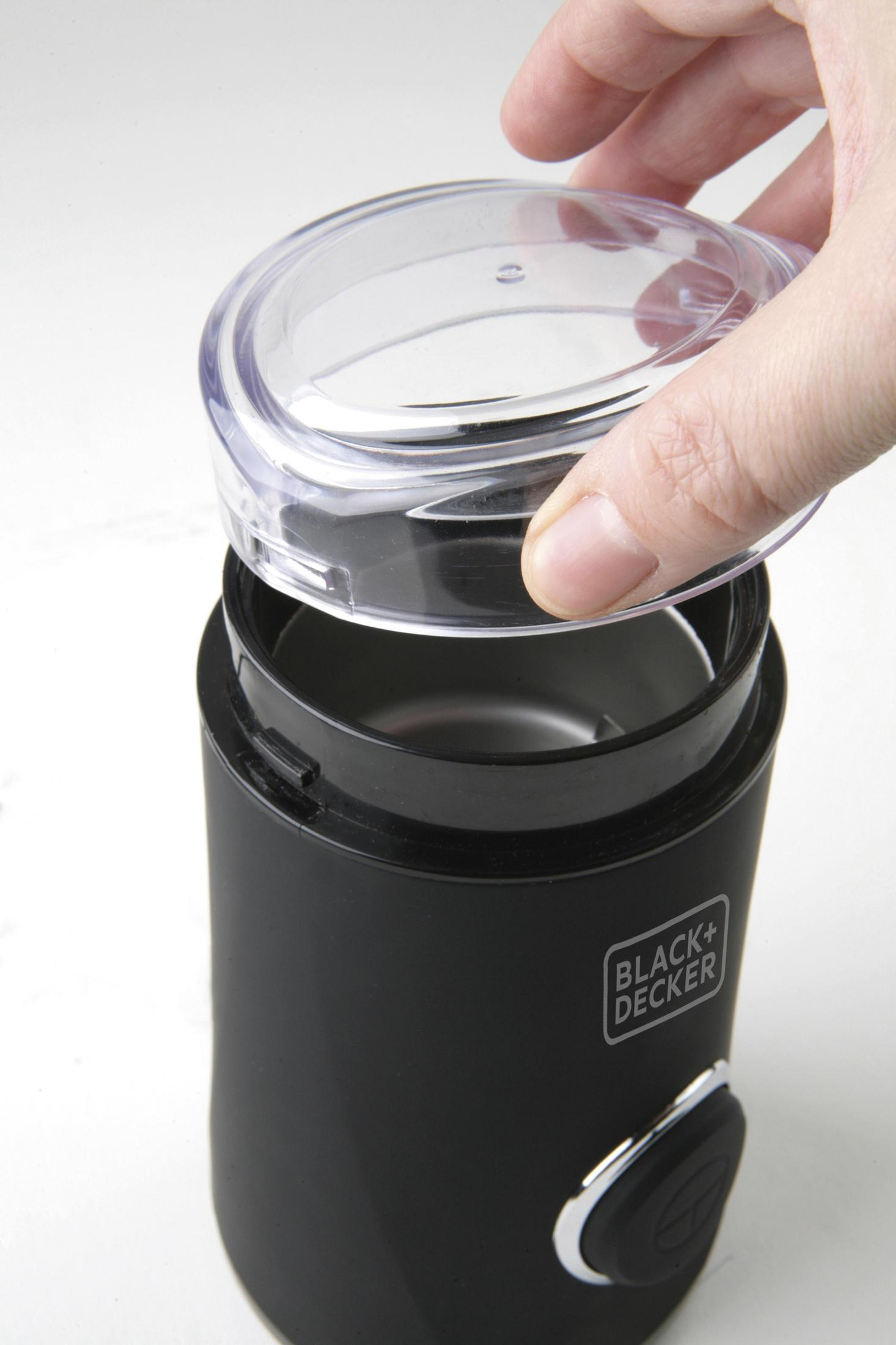 Dłoń umieszcza przezroczystą pokrywę na czarnym młynku do kawy.