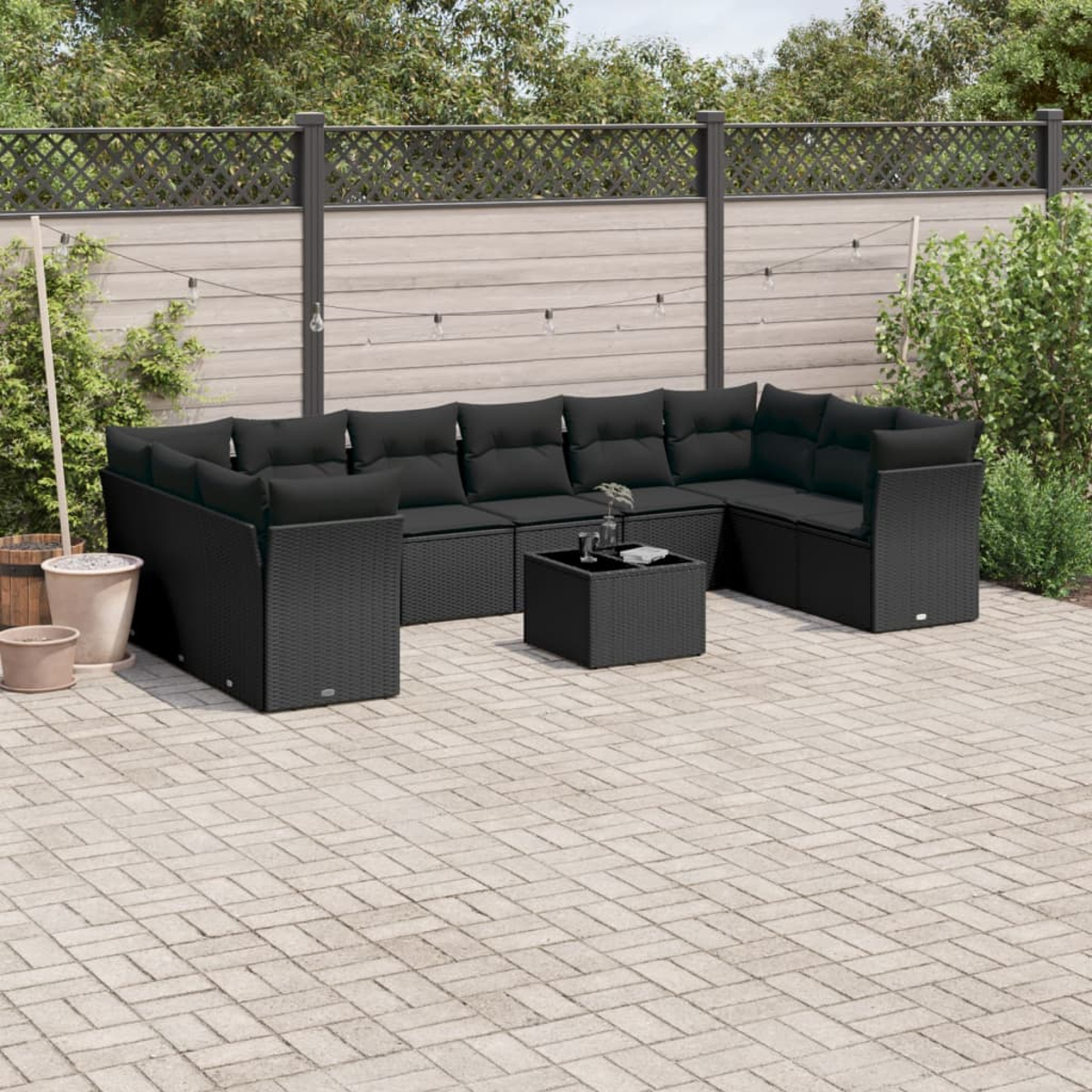 Schwarzes Outdoor-Ecksofa mit schwarzen Kissen, Couchtisch und gepflasterter Terrasse.