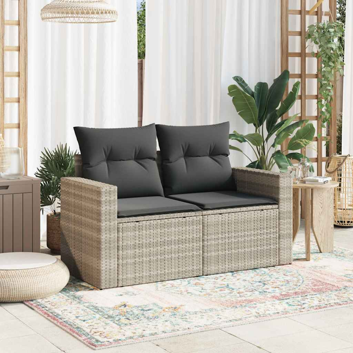 Ein zweisitziges Korbsesselsofa mit grauen Kissen. Das Sofa steht auf einem gemusterten Teppich.