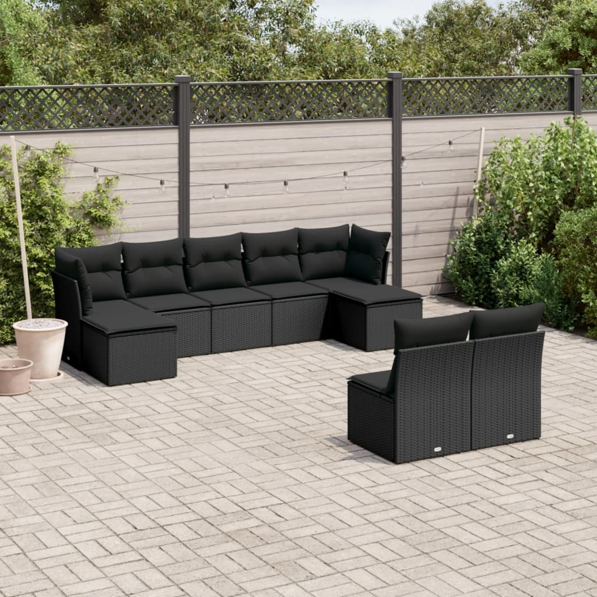 Schwarzes Outdoor-Sofa-Set aus Korbgeflecht mit schwarzen Kissen, auf einer Backstein-Terrasse.