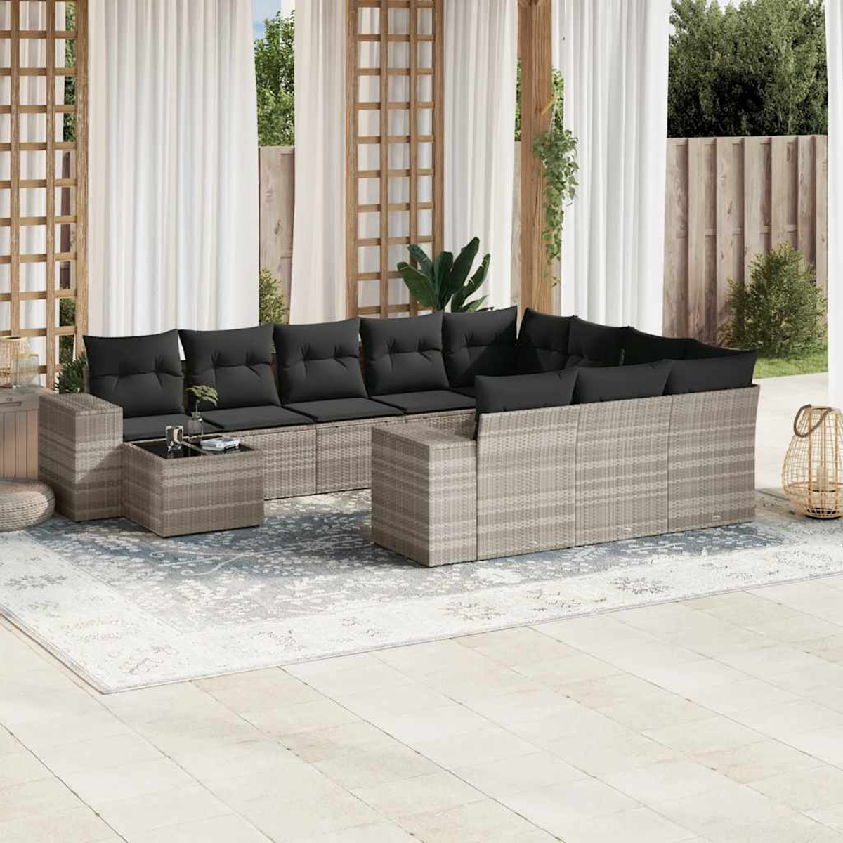 Wohnzimmer-Set im Freien. Rattan-Möbel mit schwarzen Kissen, auf einem gemusterten Teppich.