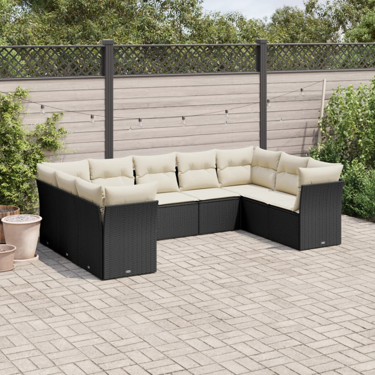 Schwarzes Rattan-U-förmiges Outdoor-Sofa mit beigefarbenen Kissen auf einer Ziegelterrasse. Hintergrund: Zaun und Pflanzen.
