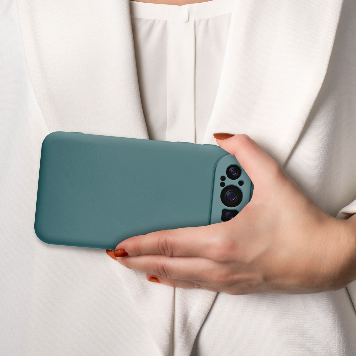 Hand einer Frau, die ein türkisfarbenes Telefon in einer Hülle hält. Weißer Blazer, neutraler Hintergrund.