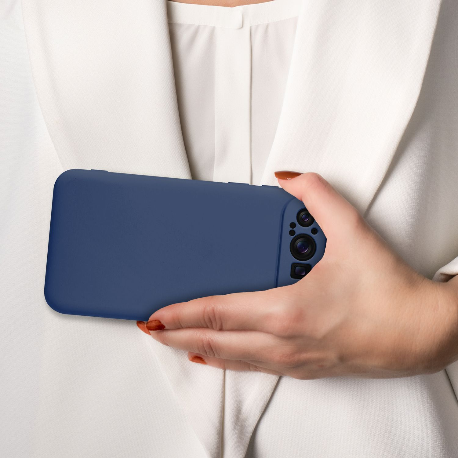 Hand einer Frau, die ein blaues Telefon in einer Hülle hält. Weißer Blazer, neutraler Hintergrund.