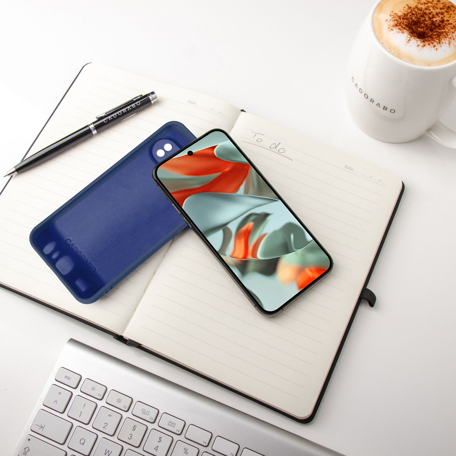 Notizbuch mit Telefon und Hülle, Stift und Tasse. Das Telefon zeigt ein farbenfrohes Bild.