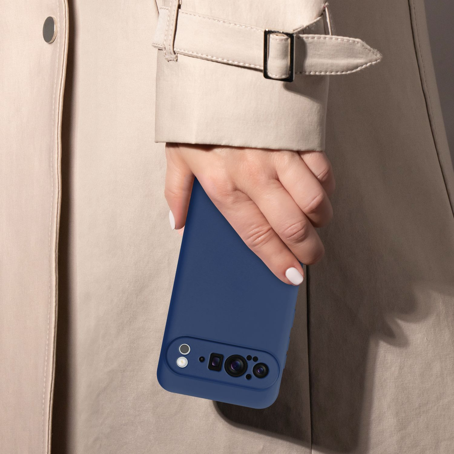 Hand einer Frau, die ein blaues Telefon in einer Hülle hält. Beiger Trenchcoat, neutraler Hintergrund.