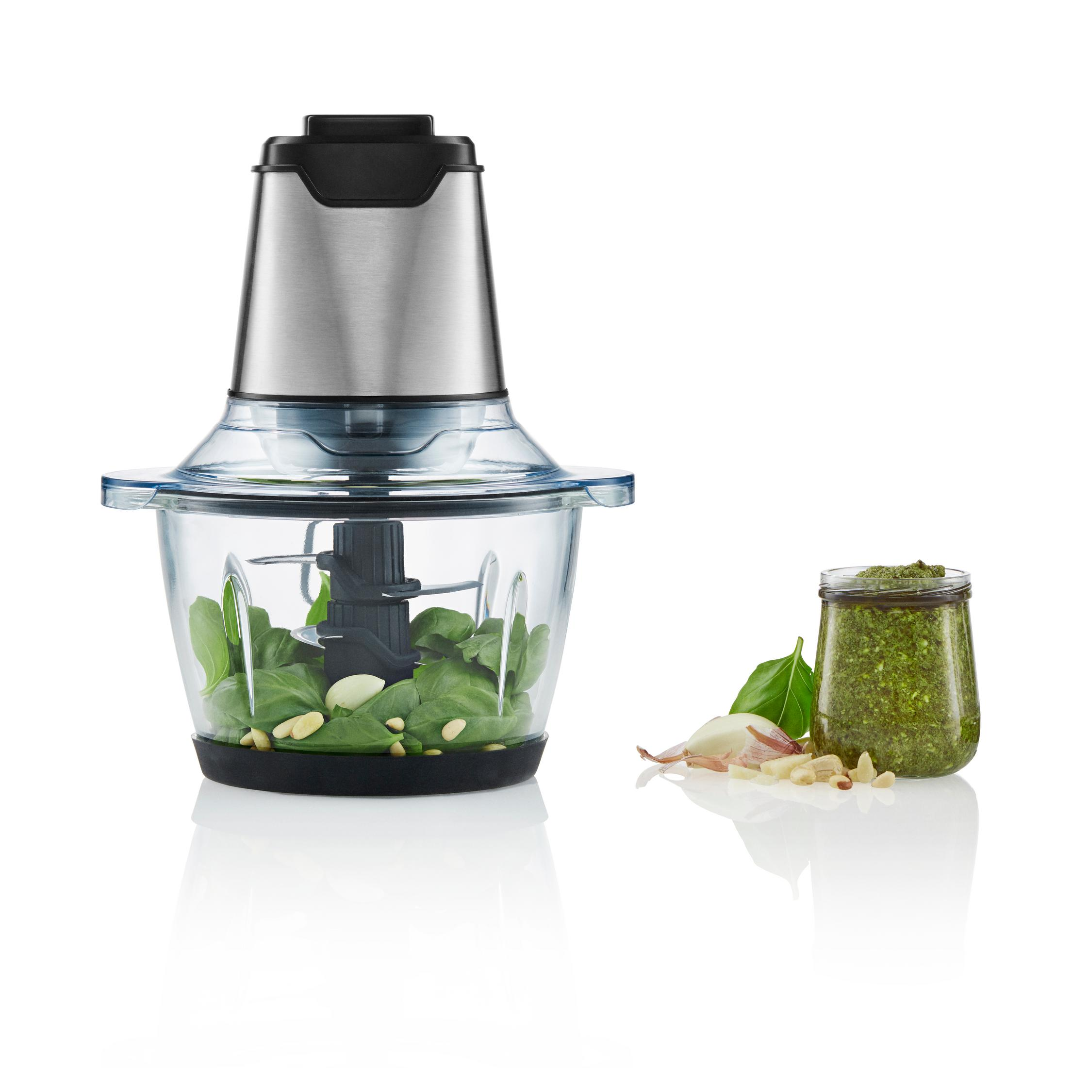 Mixer mit Basilikumblättern, Pesto im Glas und Knoblauchzehen sind sichtbar.