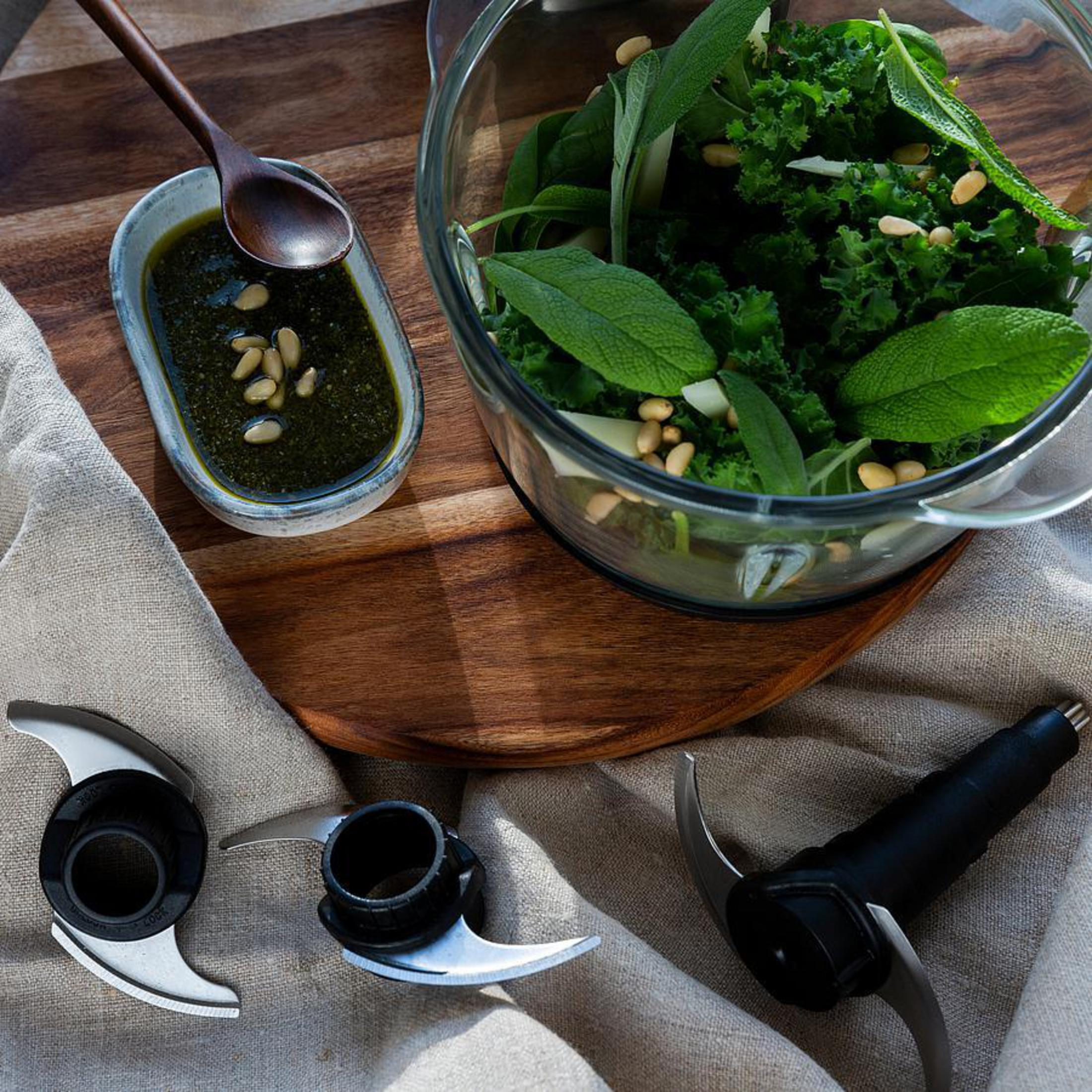 Zutaten für Pesto: Grünkohl, Pinienkerne, Salbei und Messer. Ein Löffel und Soße in einer Schüssel.
